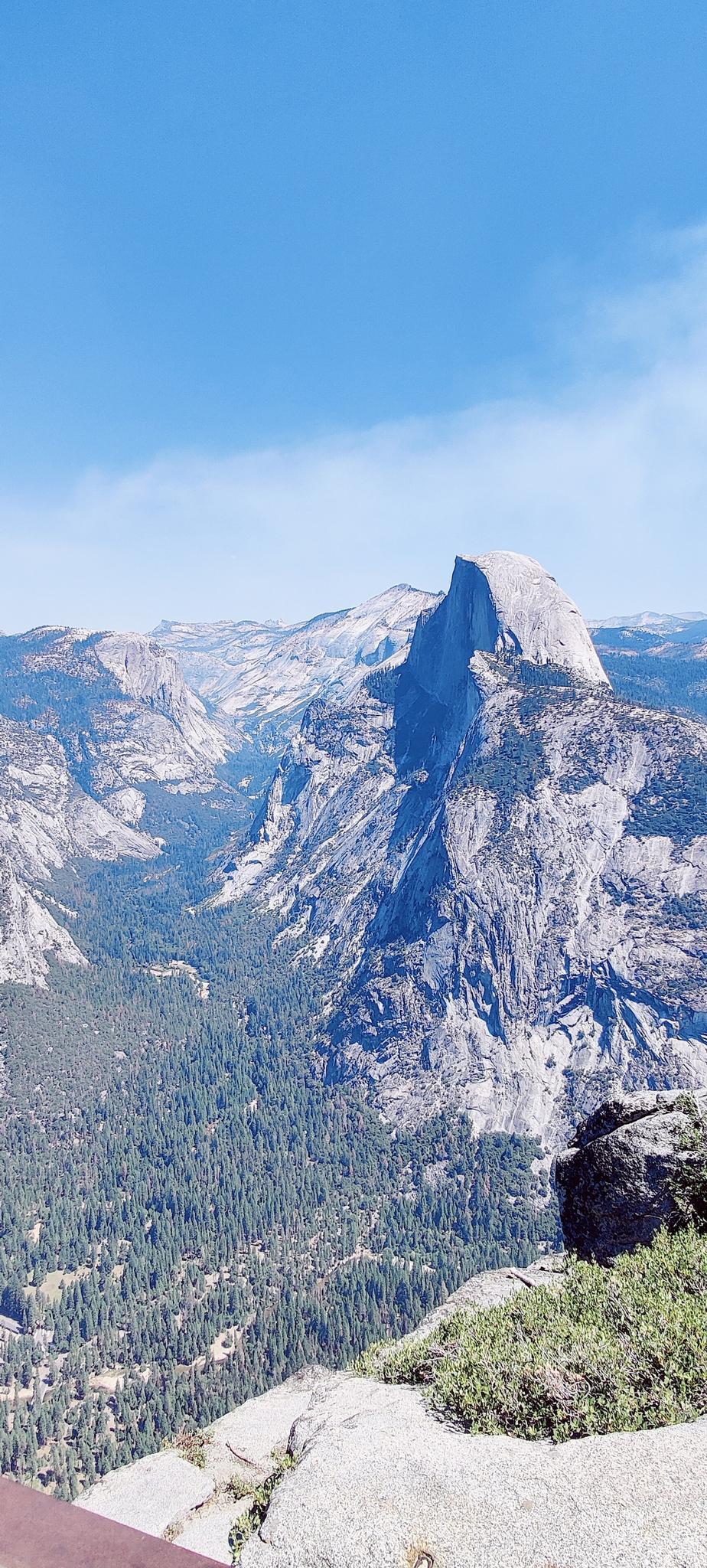 A majestic granite dome rises above a vast, forested mountain landscape.