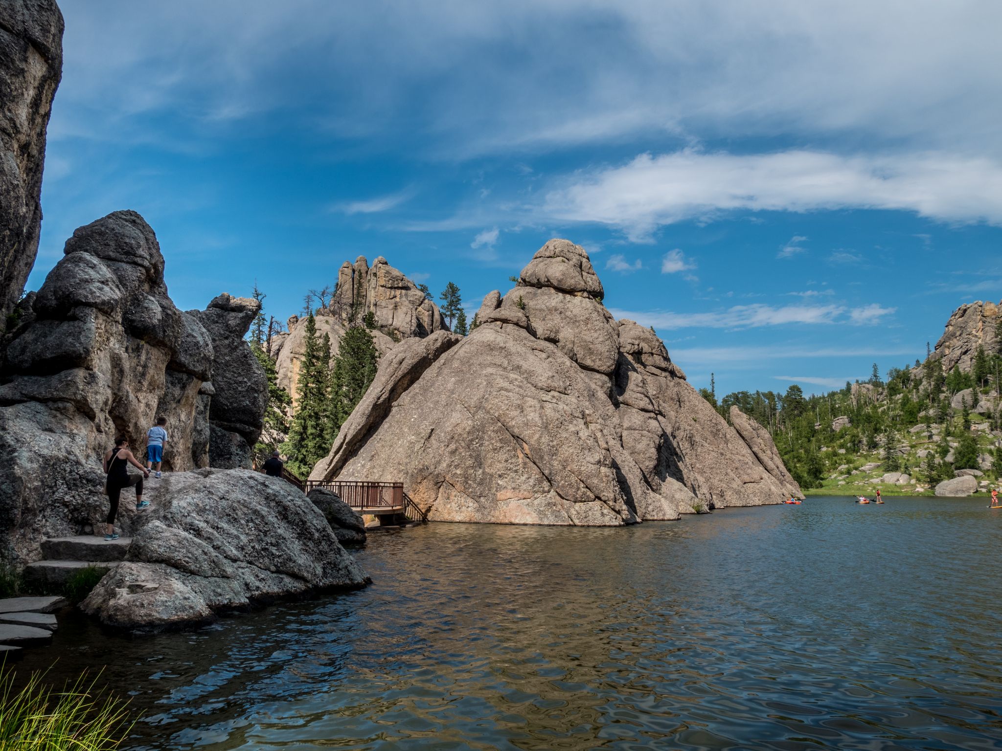 Lake with large rock formations, trees, and people on a wooden boardwalk. - Sylvan Lake – Needles Highway loop from Keystone
