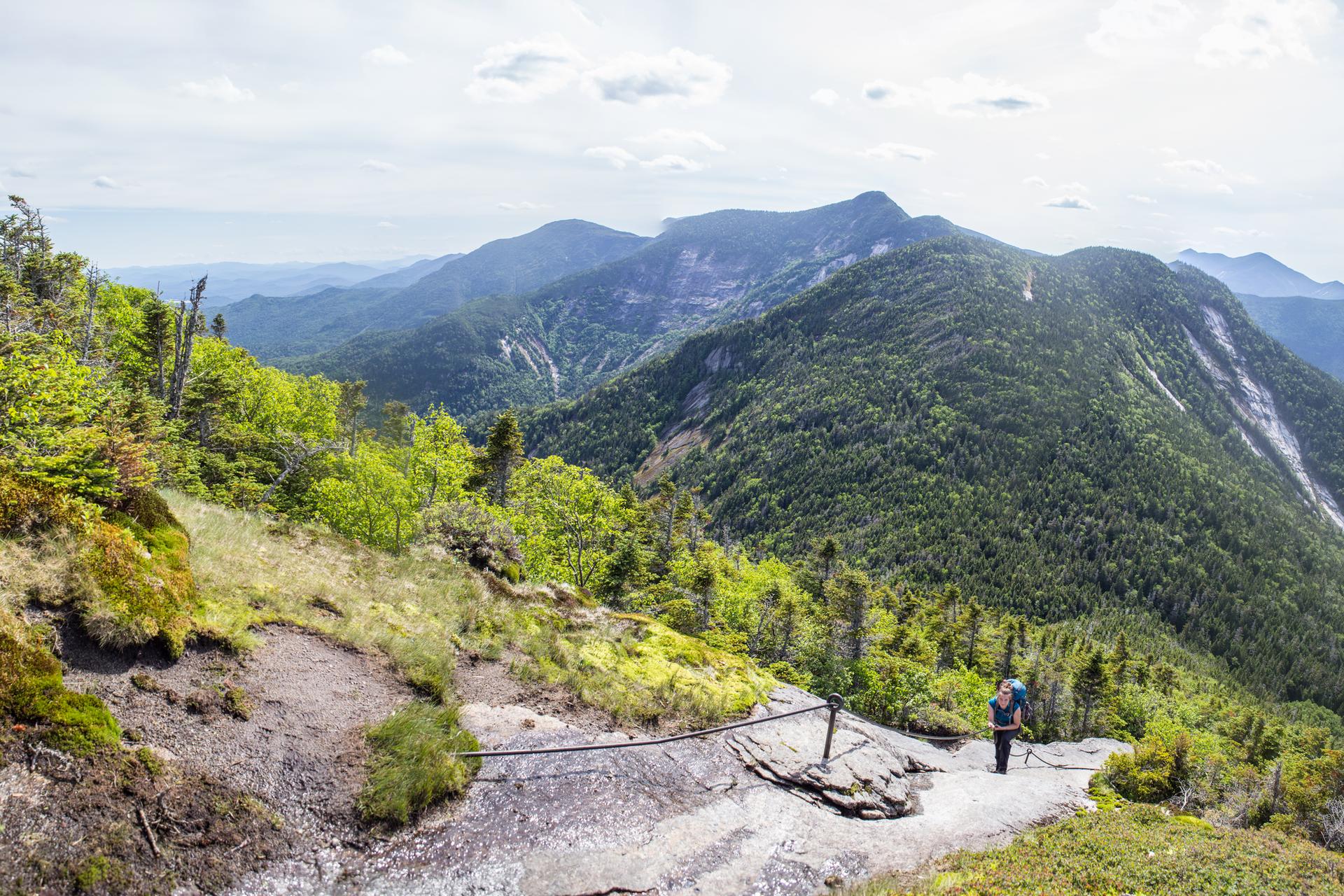 Hiker on a rocky mountain path overlooking a vast green landscape.