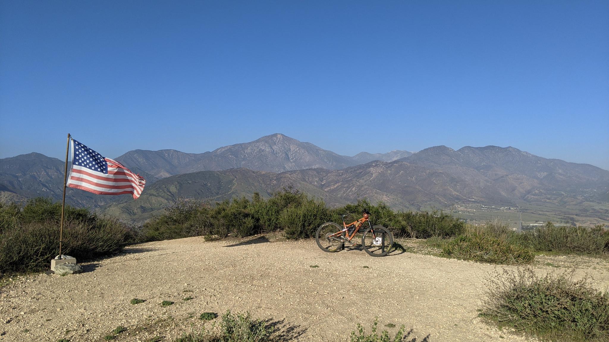 American flag and mountain bike on a hilltop overlooking vast mountains.