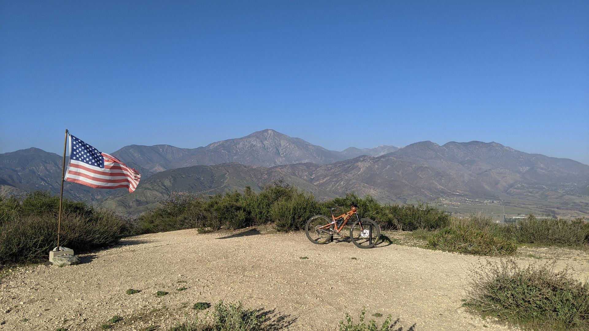 American flag and mountain bike on a hilltop overlooking vast mountains.