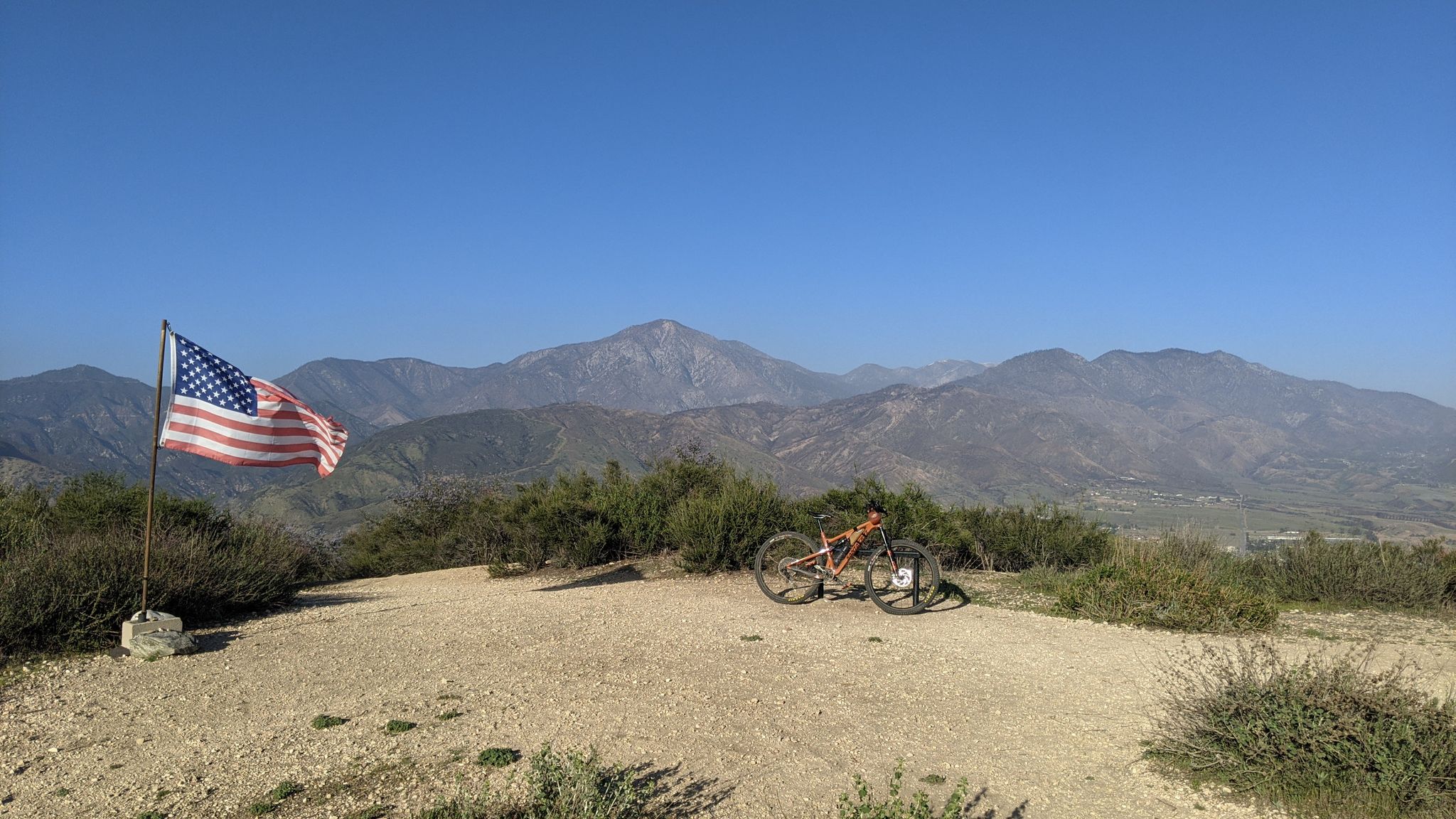 American flag and mountain bike on a hilltop overlooking vast mountains. - Crafton Hills and Zanja Peak Loop