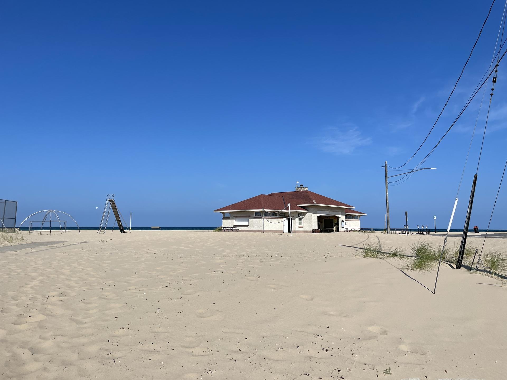 A building with a red roof stands on a wide, sunny sandy beach.