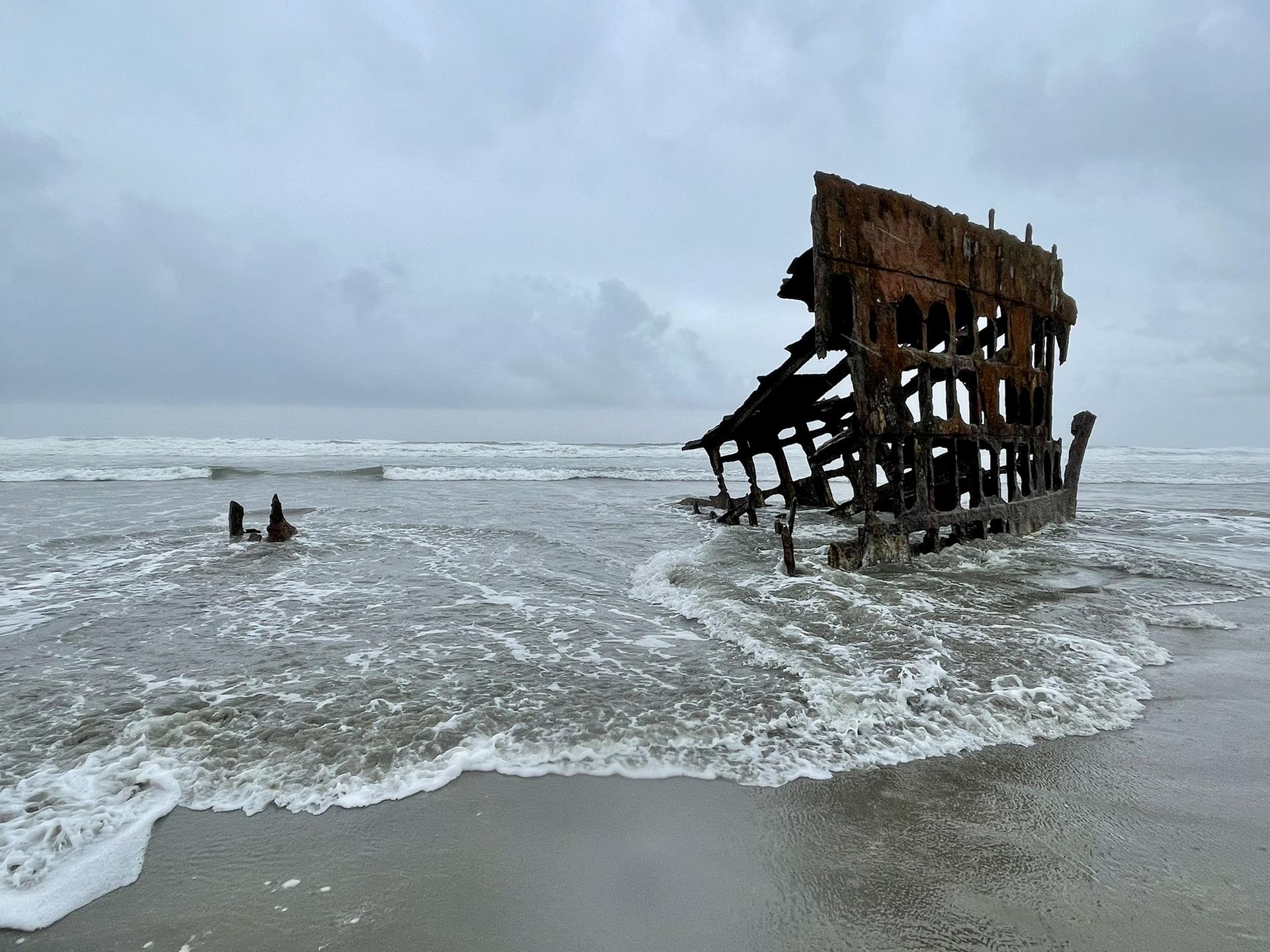Rusty shipwreck remains on a sandy beach under an overcast sky.