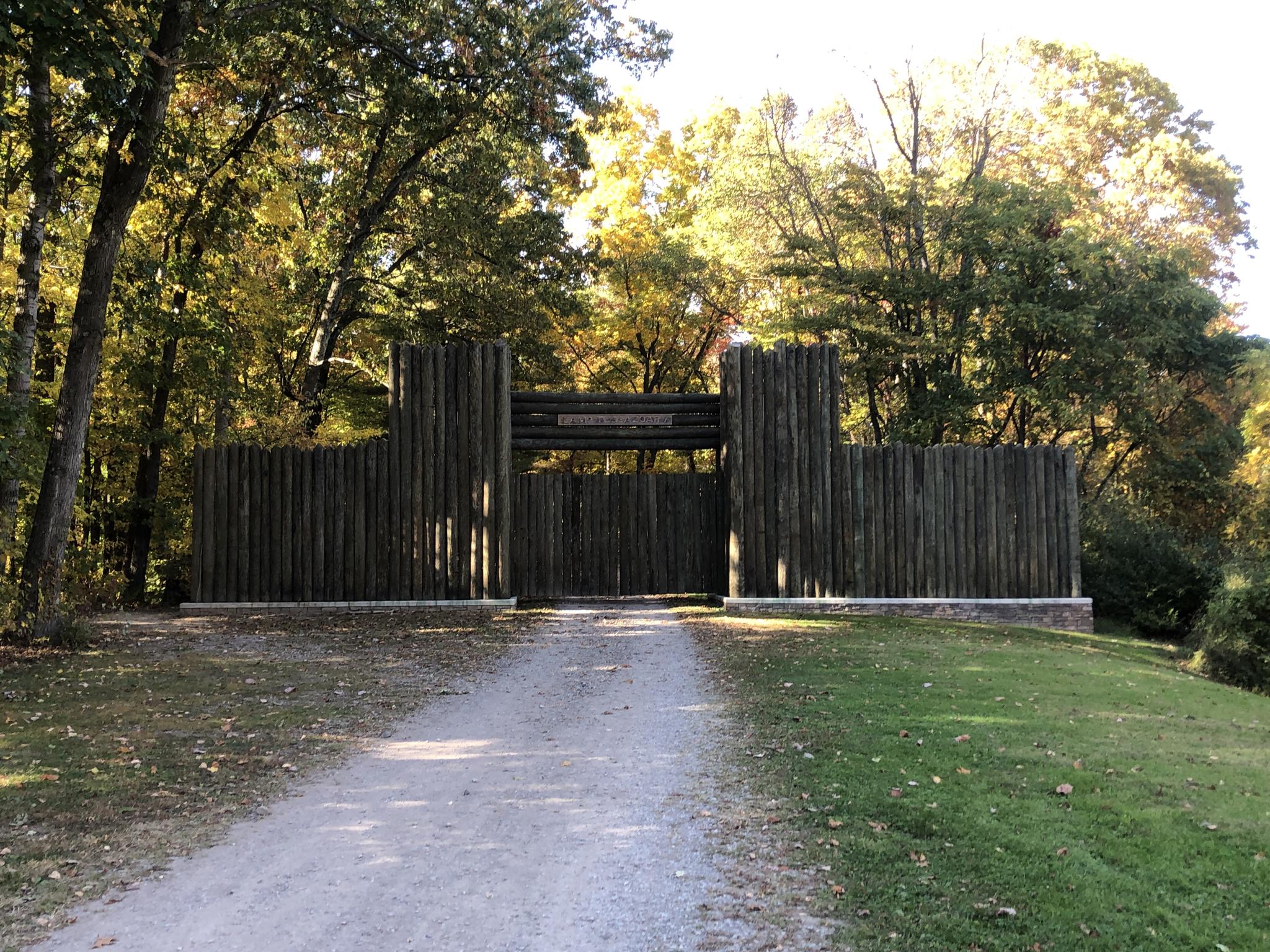 Large wooden palisade wall and gate at the end of a gravel path.