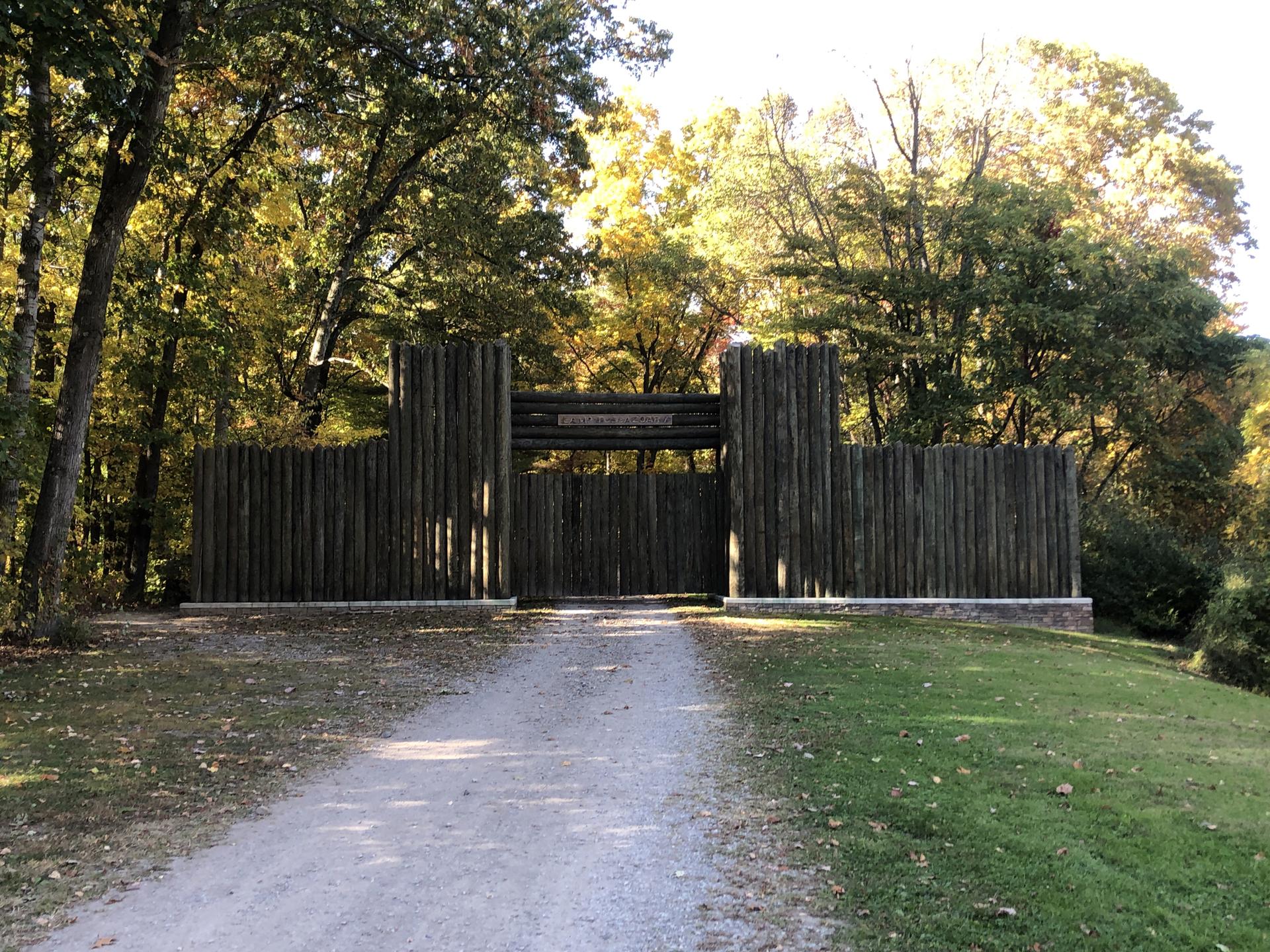 Large wooden palisade wall and gate at the end of a gravel path.