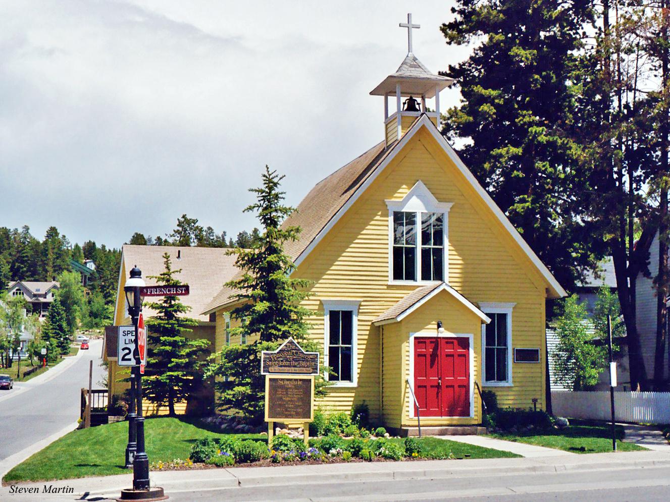 Bright yellow church with red doors and bell tower on a sunny day.