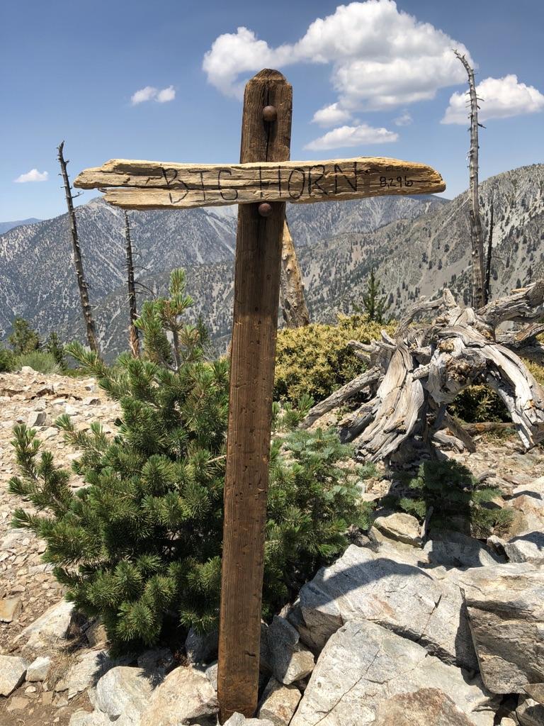 Wooden signpost on a rocky mountain peak under a cloudy sky.