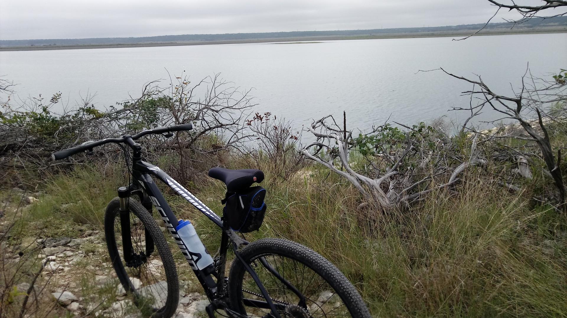 Mountain bike on a grassy bank overlooking a calm lake under an overcast sky.
