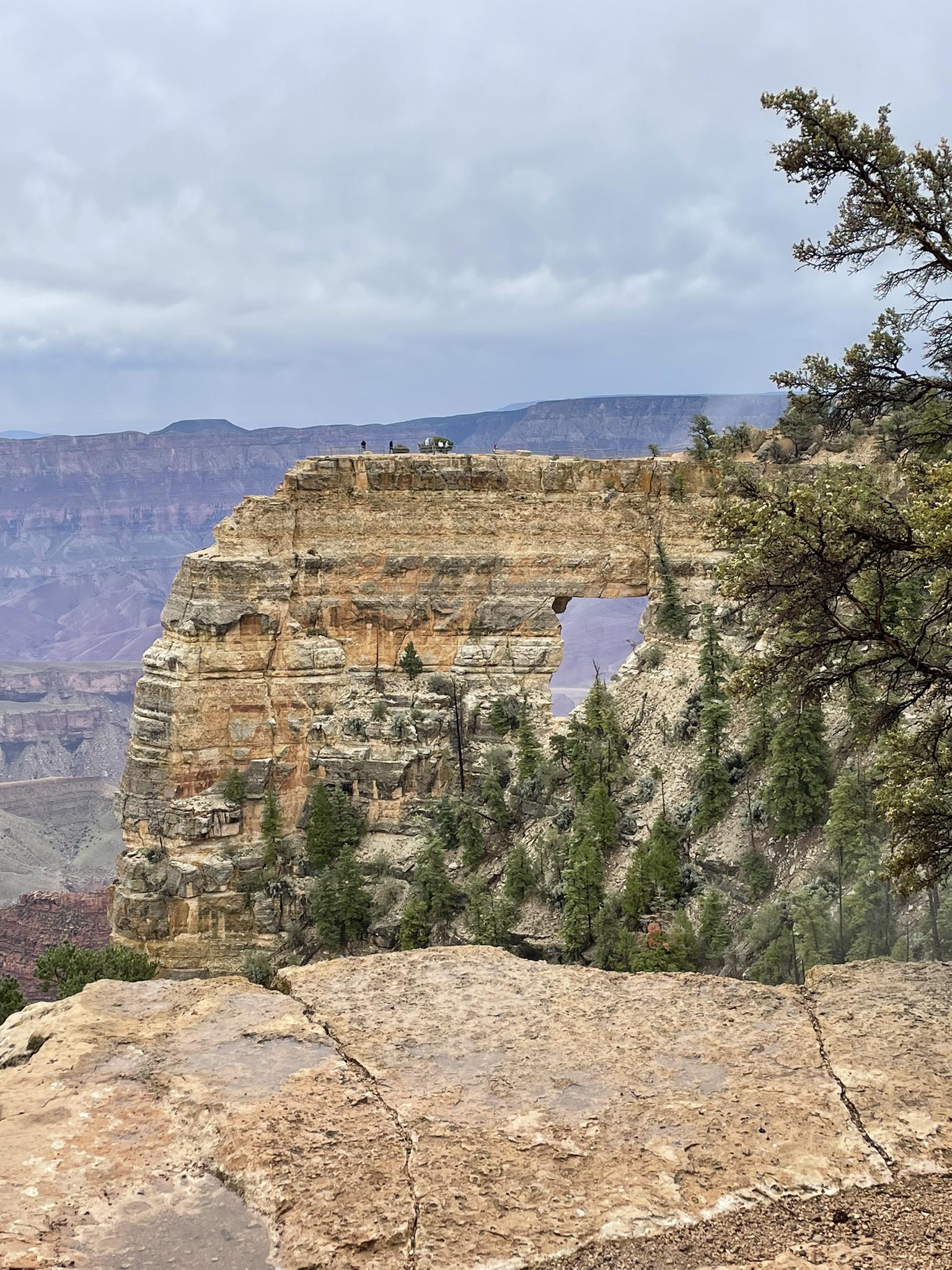 Overcast view of a natural rock arch with distant people on top.