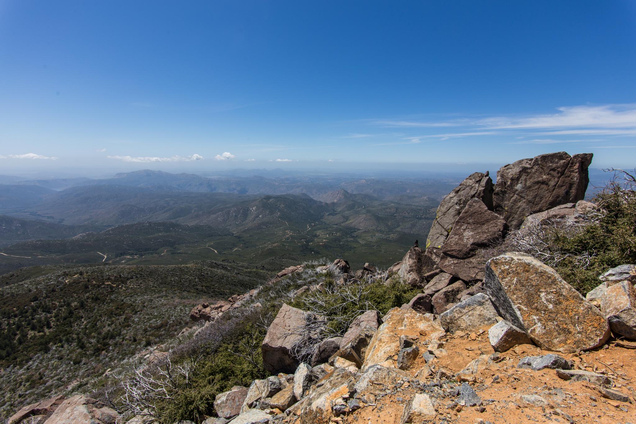 Panoramic view of rugged mountains under a clear blue sky. Large rocks in foreground.