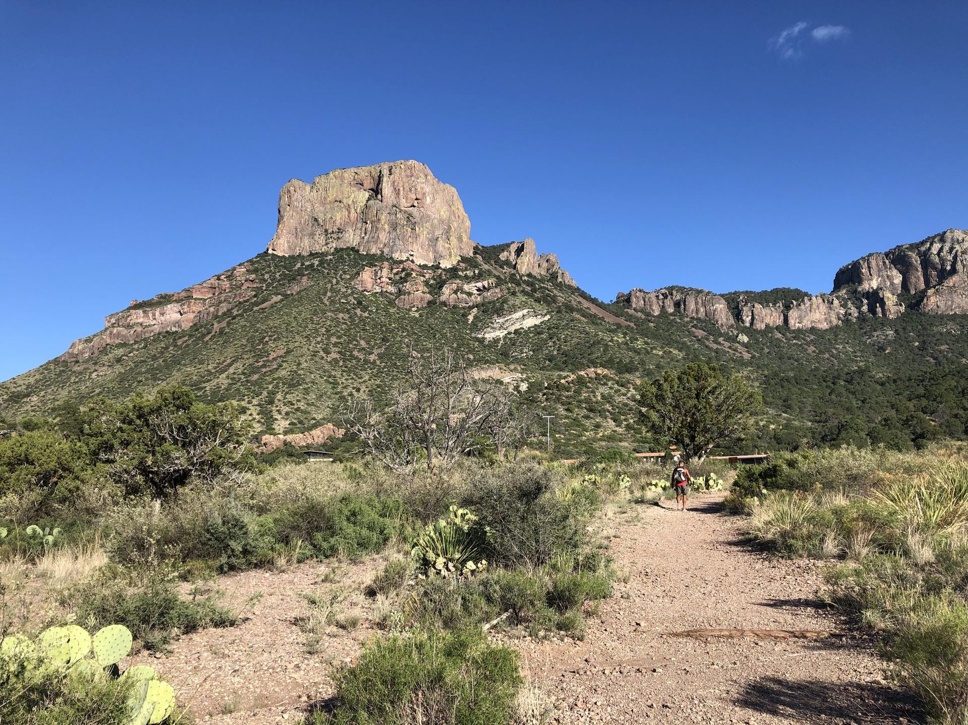 Hiker on a dirt path with a large, flat-topped mountain in the background.