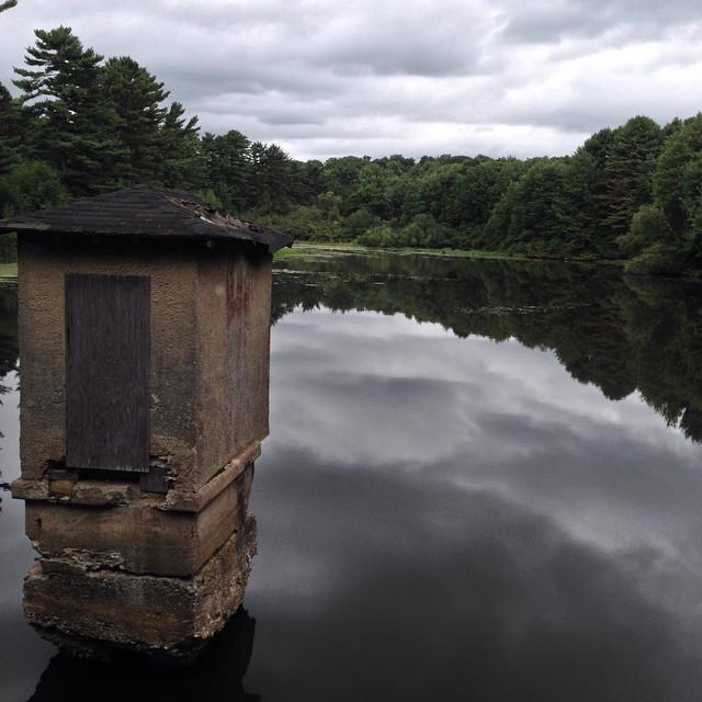 A weathered stone building in still water reflects a cloudy sky.