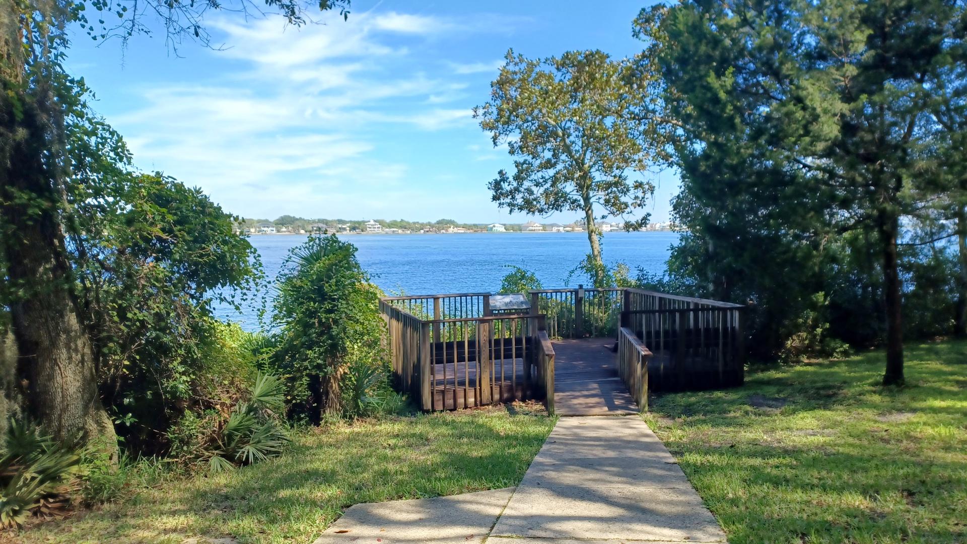 Wooden observation deck overlooking a wide blue body of water on a sunny day.