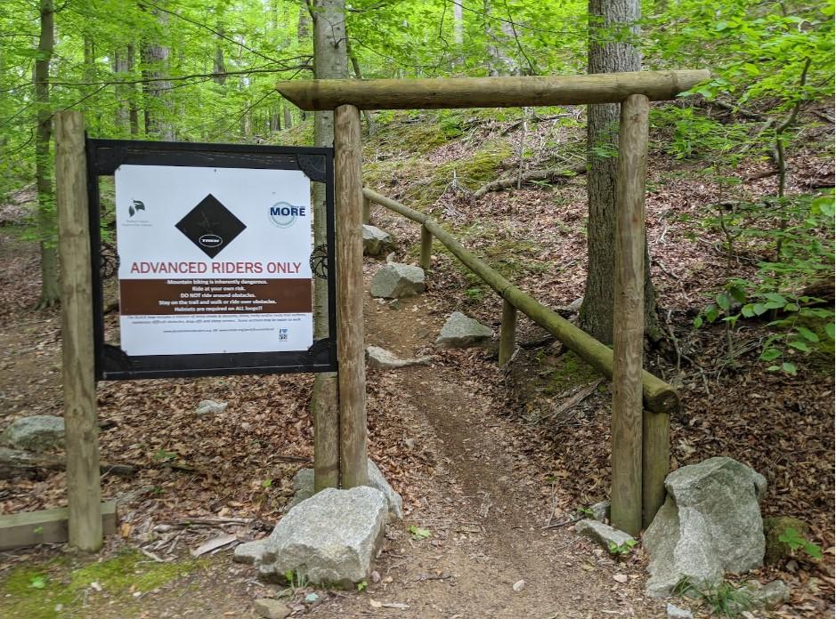 A trail entrance with an 'Advanced Riders Only' sign and wooden archway.