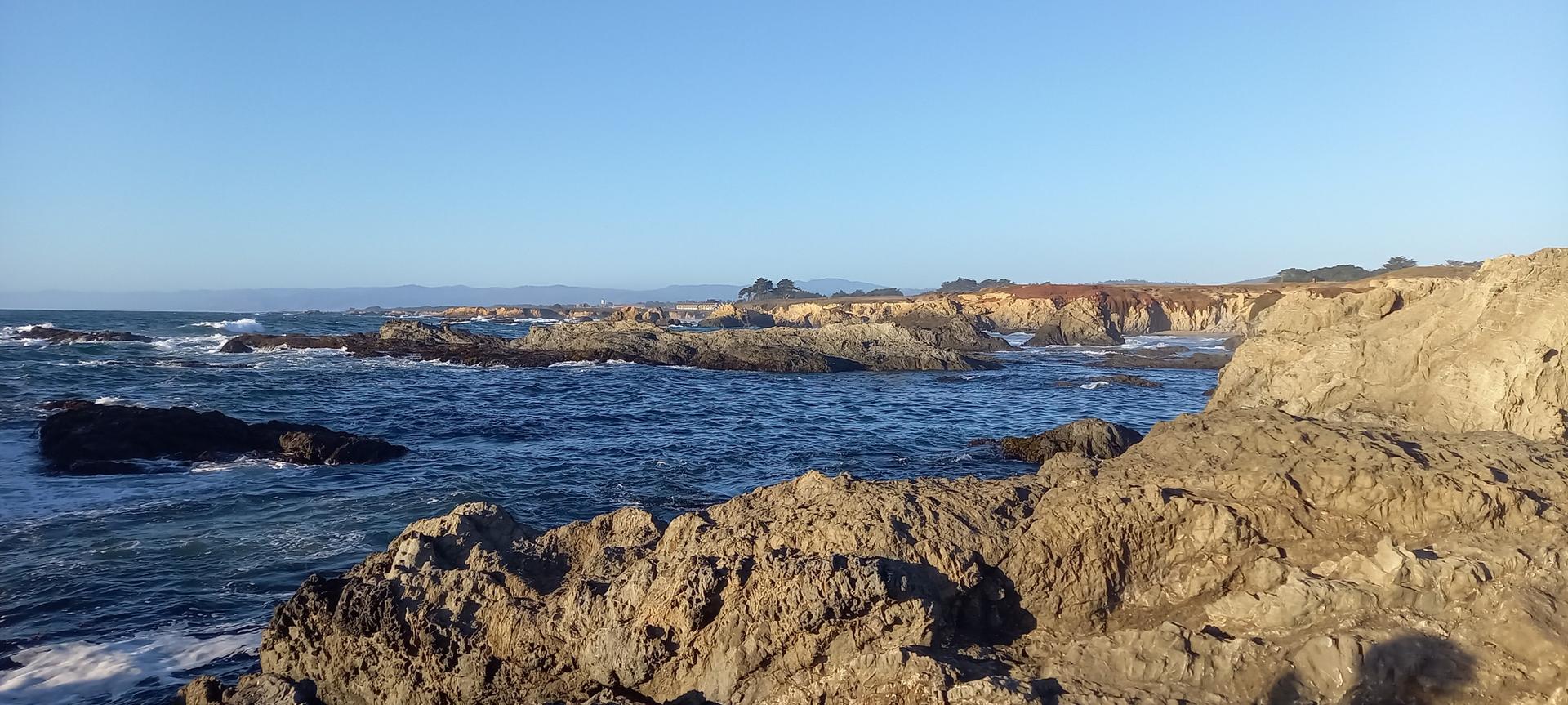 Sunny view of rugged rocky coastline with crashing ocean waves.