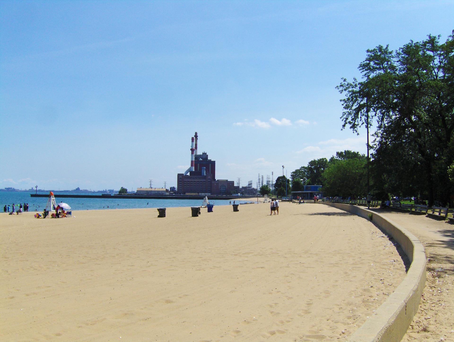 Wide sandy beach with people, large building, and blue sky.