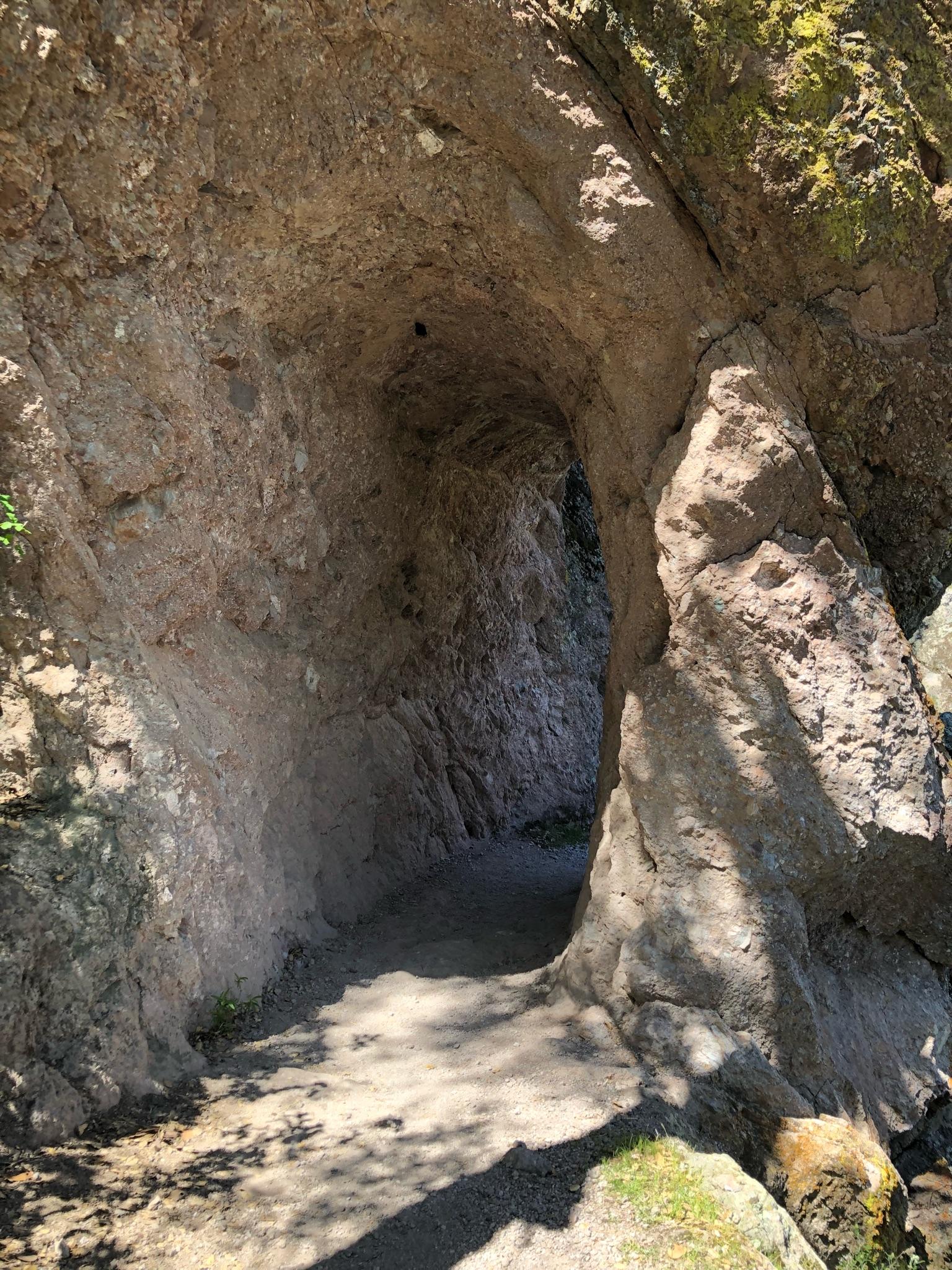 A narrow, dark rock tunnel with a path, lit by sunlight at the entrance.