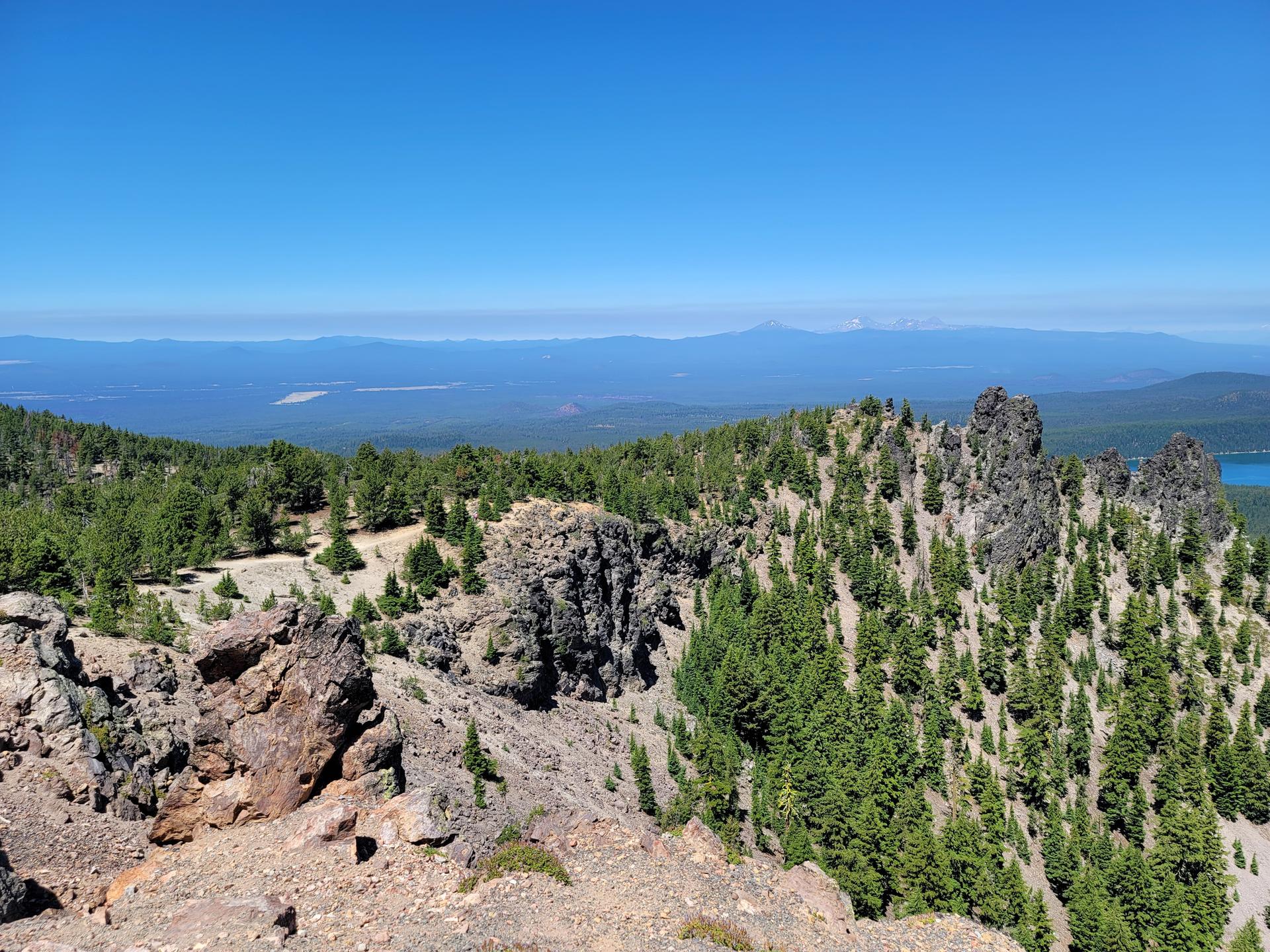Rugged rocky peaks and green pine trees on a mountain ridge under clear blue sky.