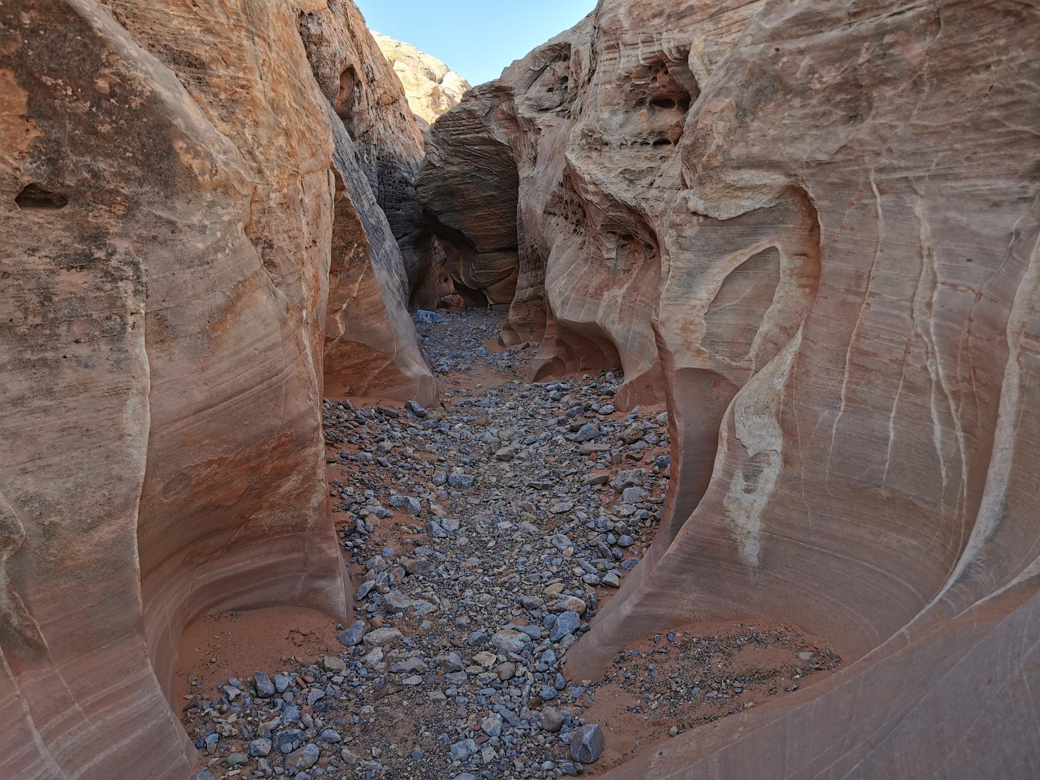 Deep, narrow slot canyon with smooth, layered rock walls and a rocky floor.