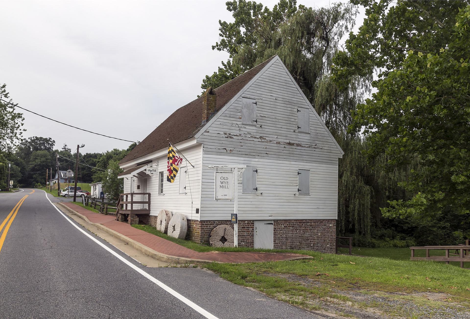 Weathered white wooden building with a flag next to a paved road on an overcast day.