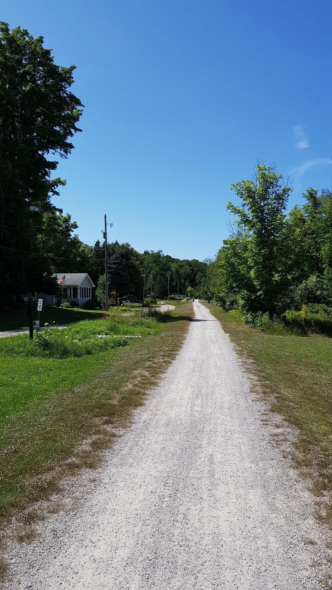 Long, straight gravel path bordered by green trees and grass on a sunny day.