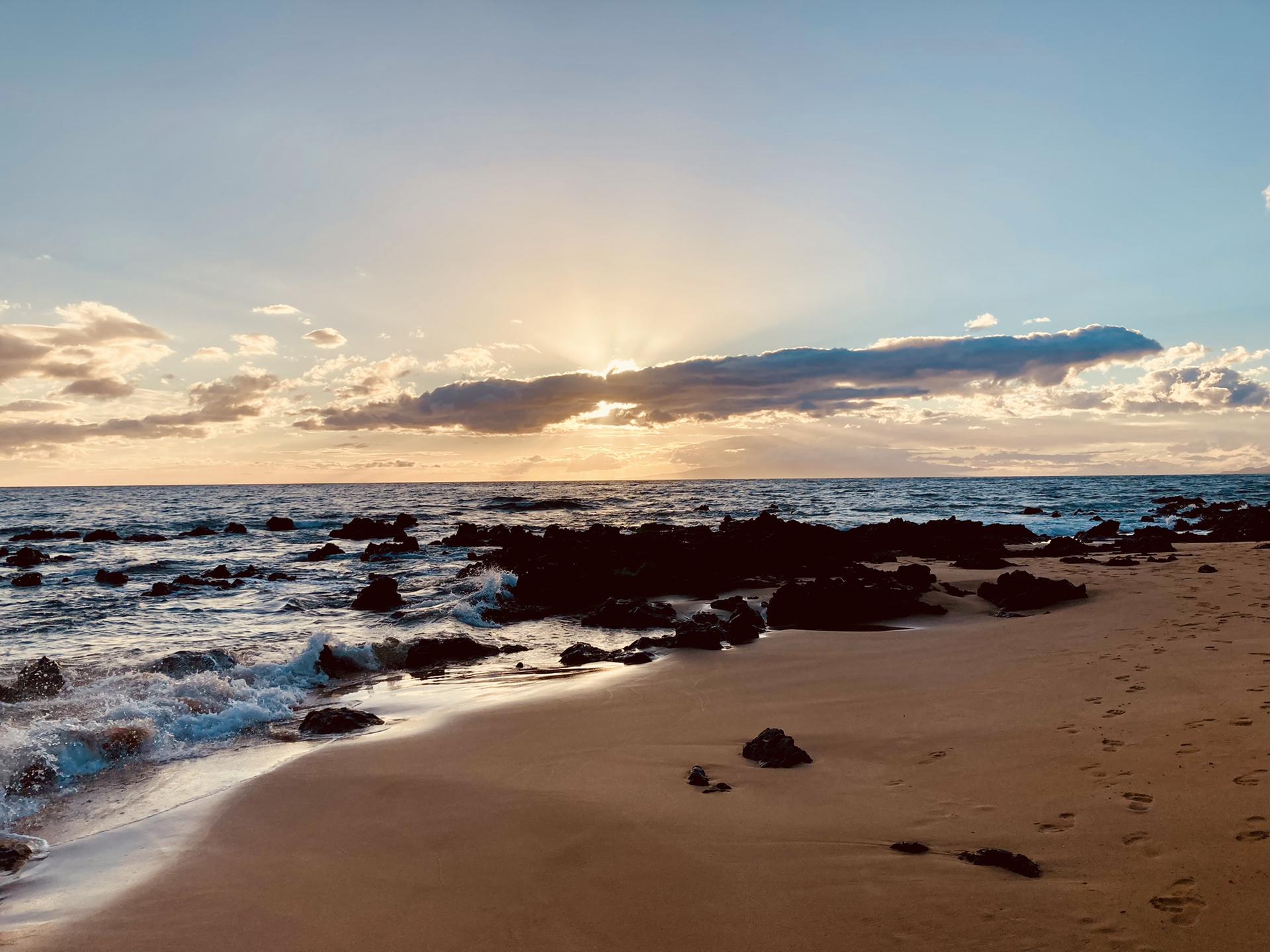 Sunset over a rocky beach with waves crashing and golden light.