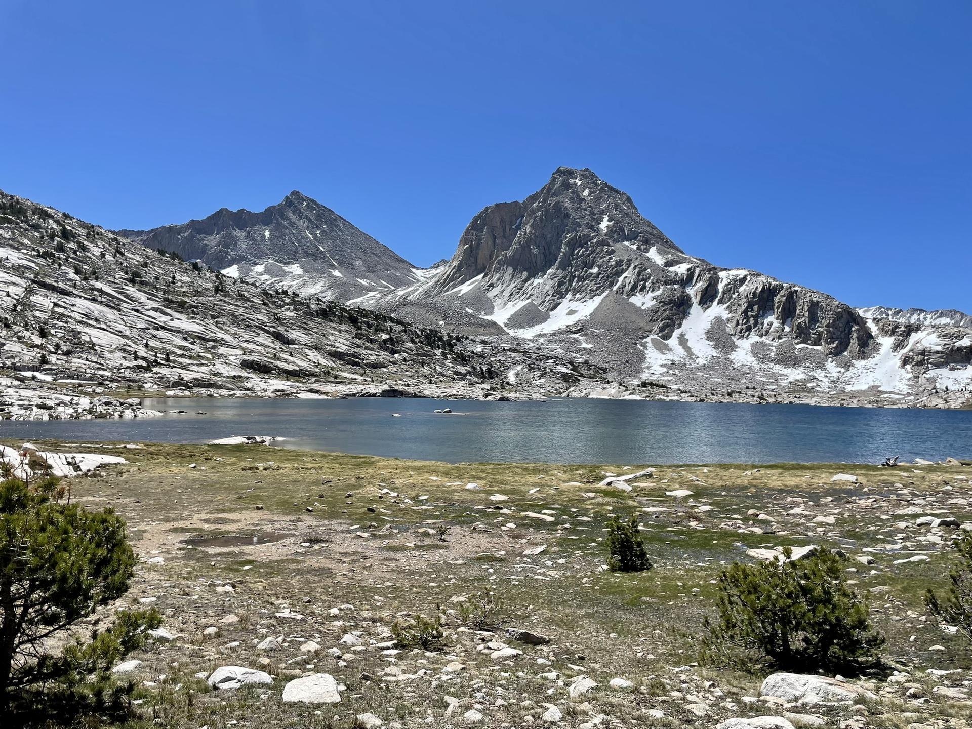A serene mountain lake with snow-capped peaks under a bright blue sky.