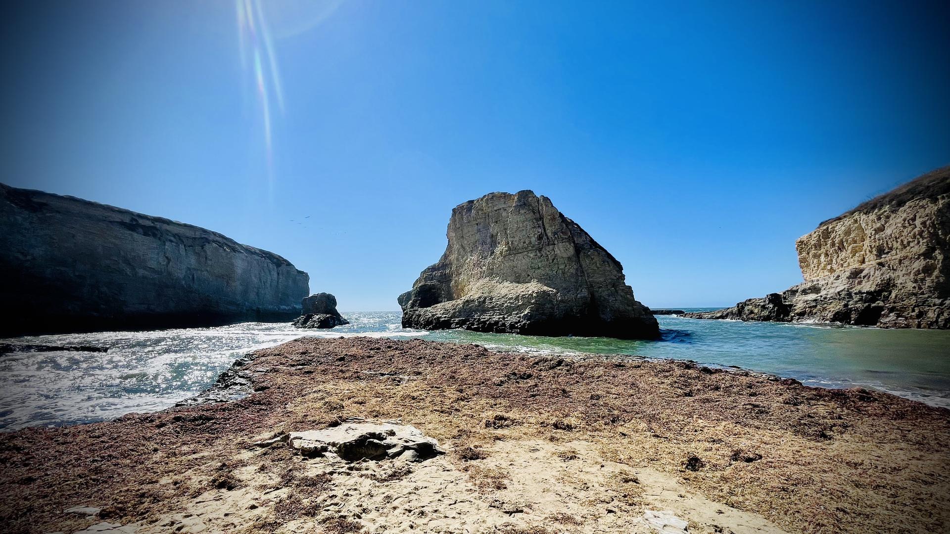 Sunny coastal view with a large sea stack, ocean, and rocky foreground.