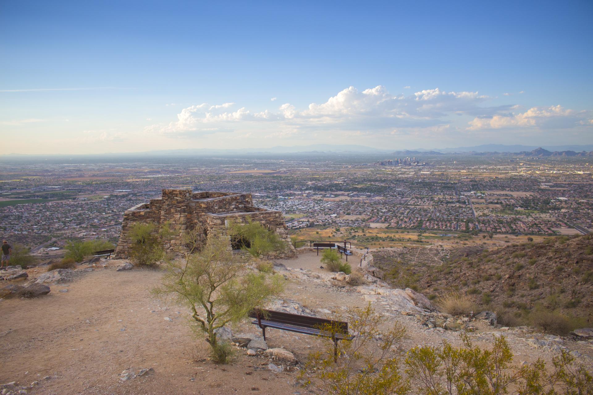 Stone structure on a desert hilltop overlooking a vast city at dusk.