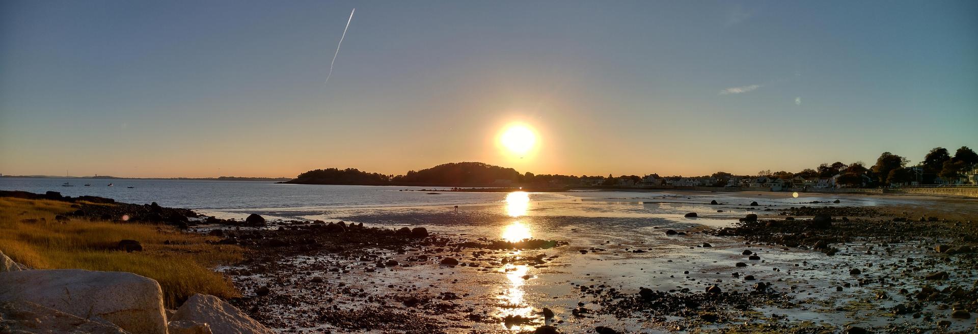 Panoramic sunset over a low tide bay with exposed rocks and a distant island.