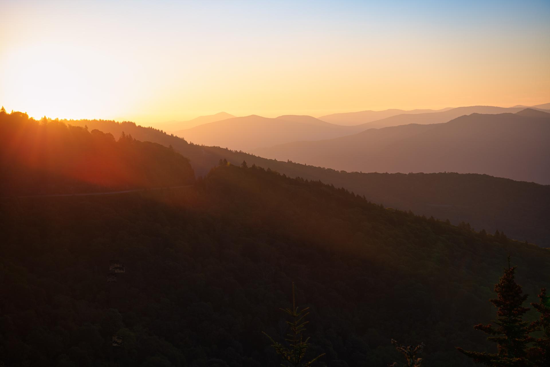 Golden sunset over layered mountain ranges, casting warm light.