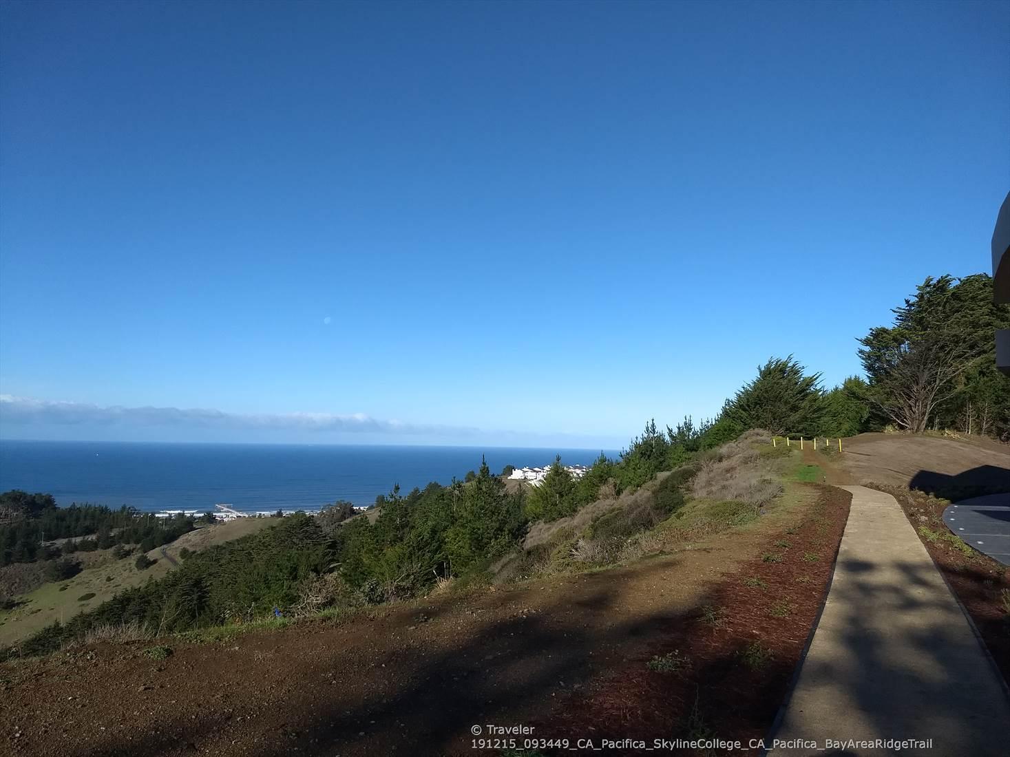 A paved path winds along a green hillside overlooking the vast ocean.