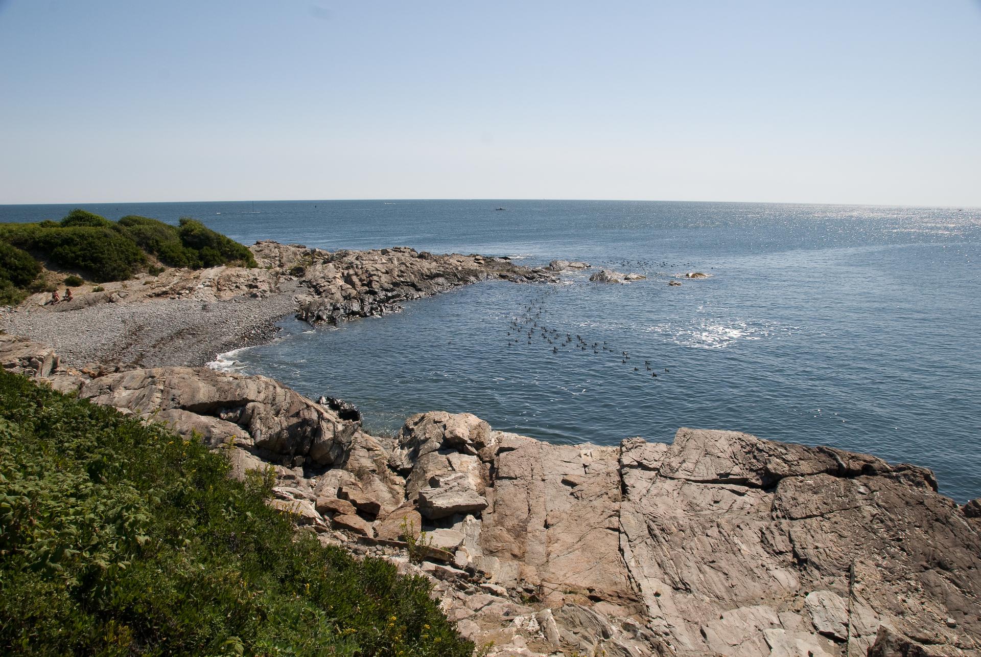 Rocky coastline with a small pebble beach and calm blue ocean on a sunny day.