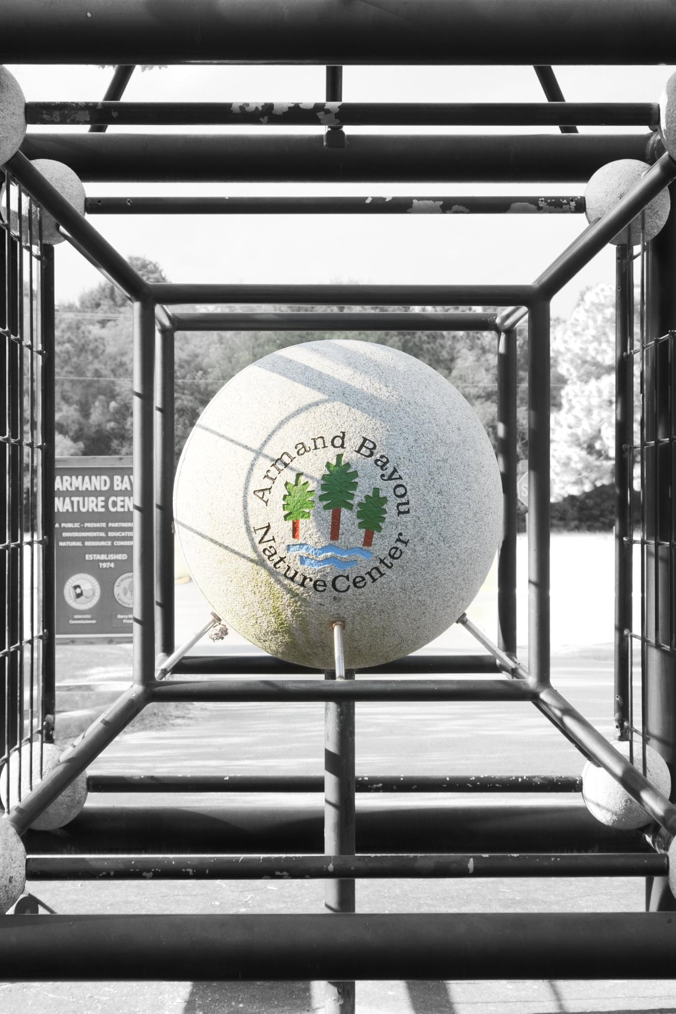 A large spherical stone with a logo sits inside a metal cube structure outdoors.