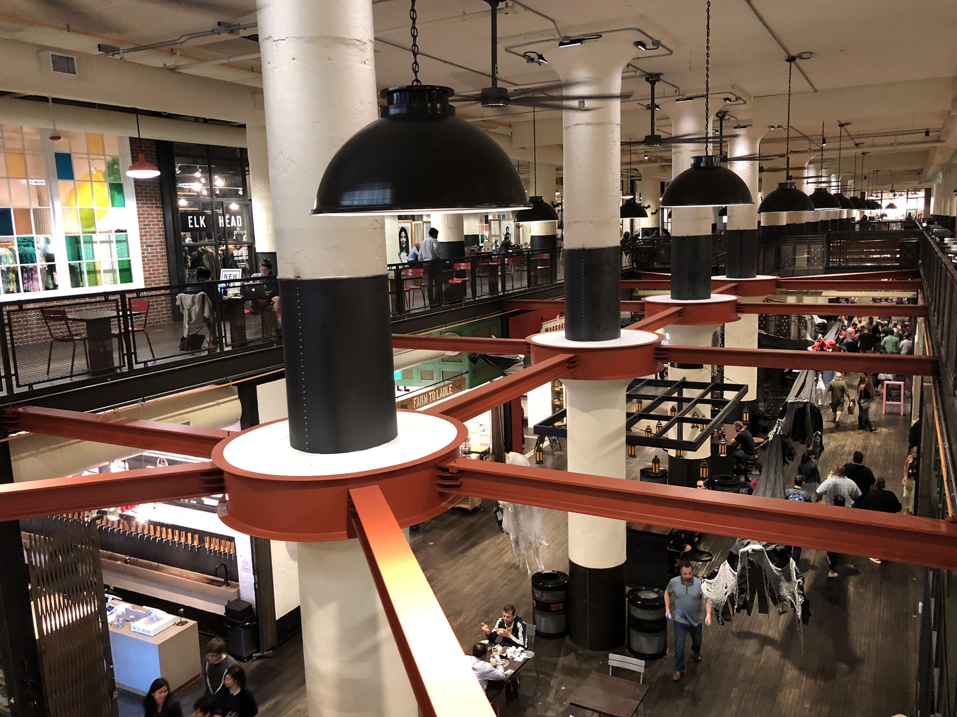 Busy multi-level indoor market with people dining and walking under large lights.