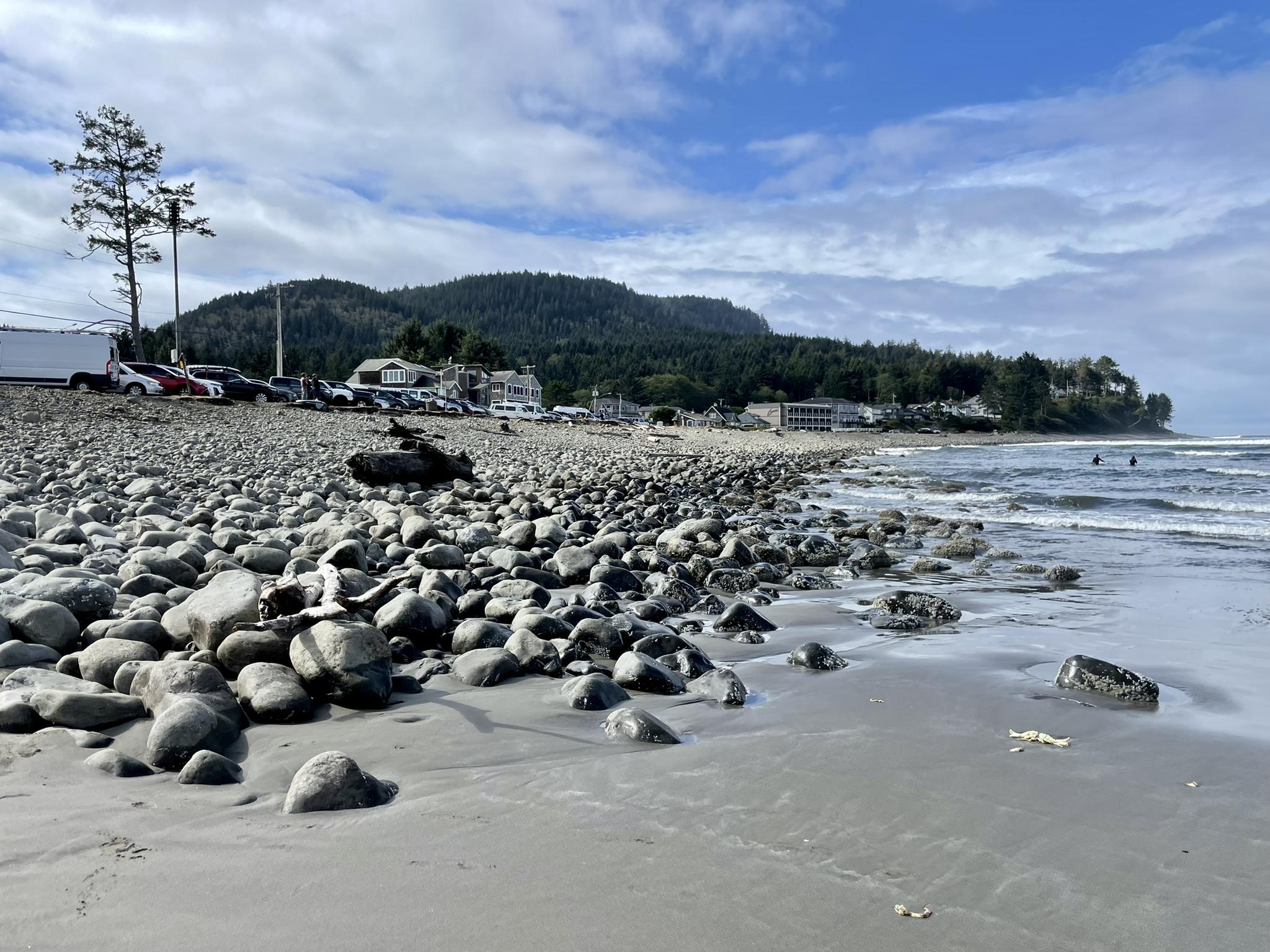 Rocky and sandy beach with ocean waves, distant town, and people swimming.