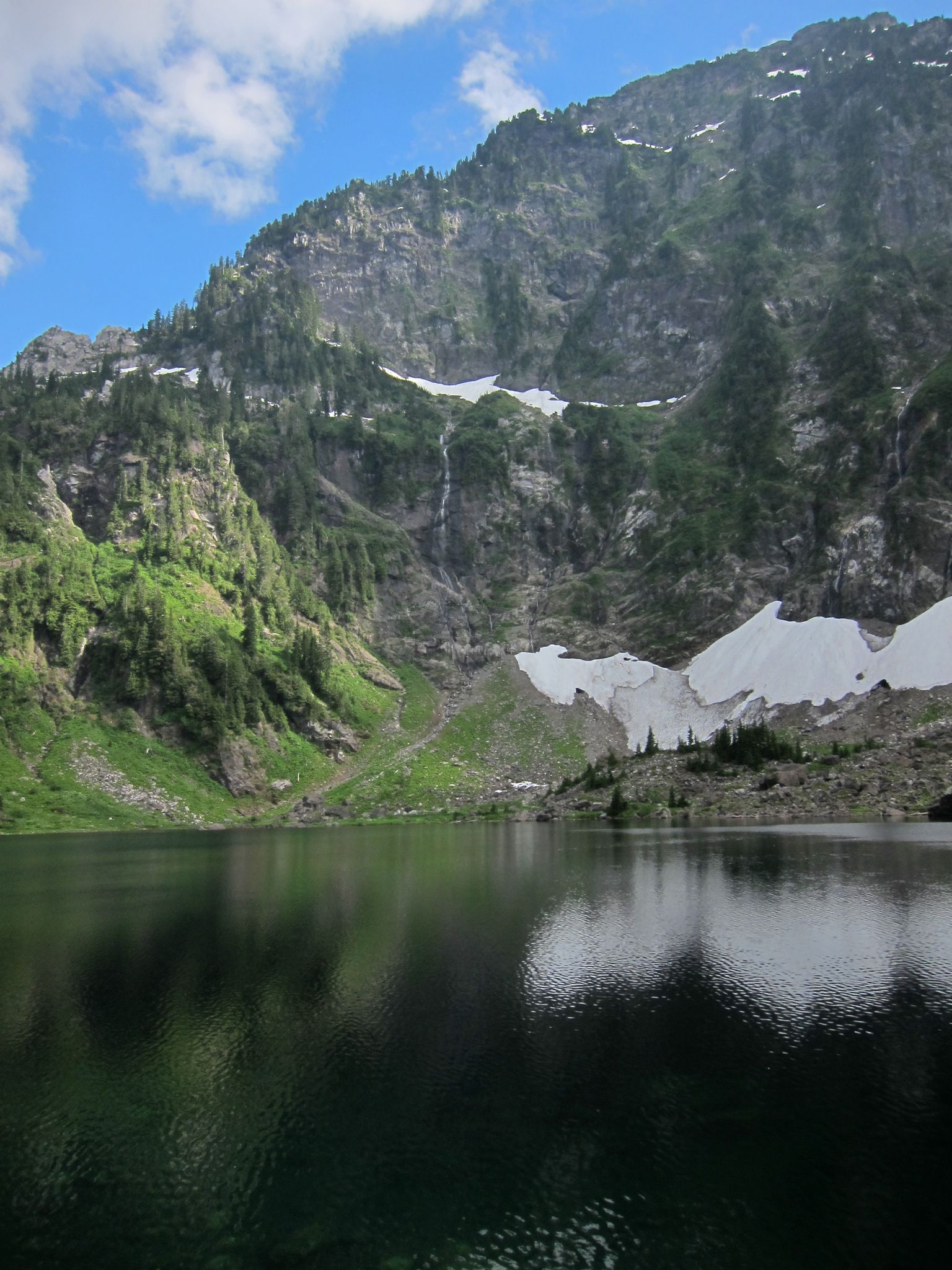 Serene lake reflecting green and rocky mountains under a bright blue sky. - Lake Twenty Two Trail