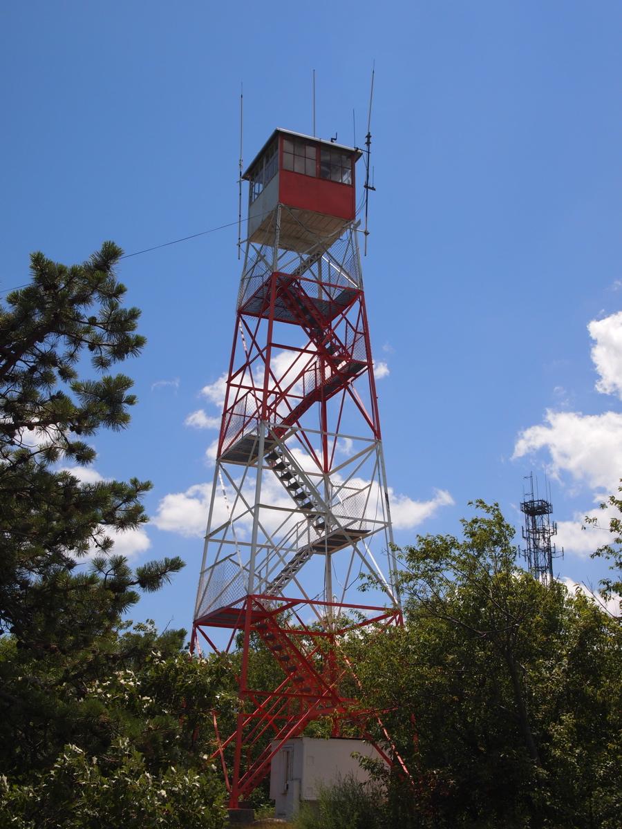 Tall red and white fire lookout tower against a blue sky.