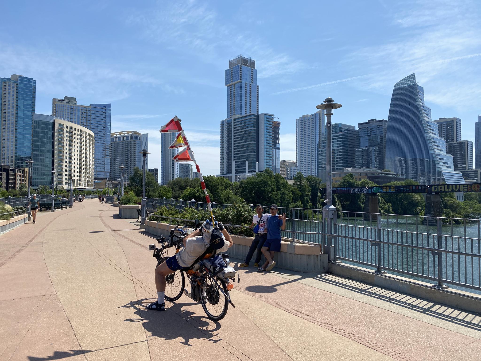 Sunny day with a recumbent bike, people, and a modern city skyline.
