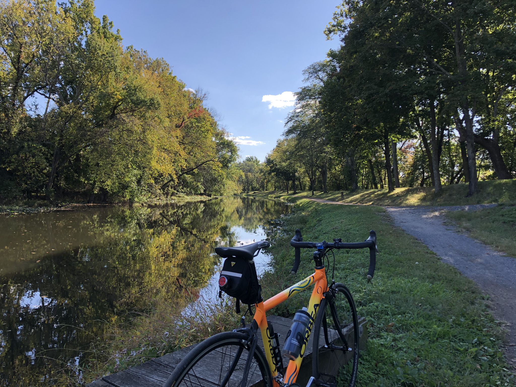 Bicycle parked beside a calm canal with reflections under a sunny sky. - D&R Canal Towpath loop from Mercer County