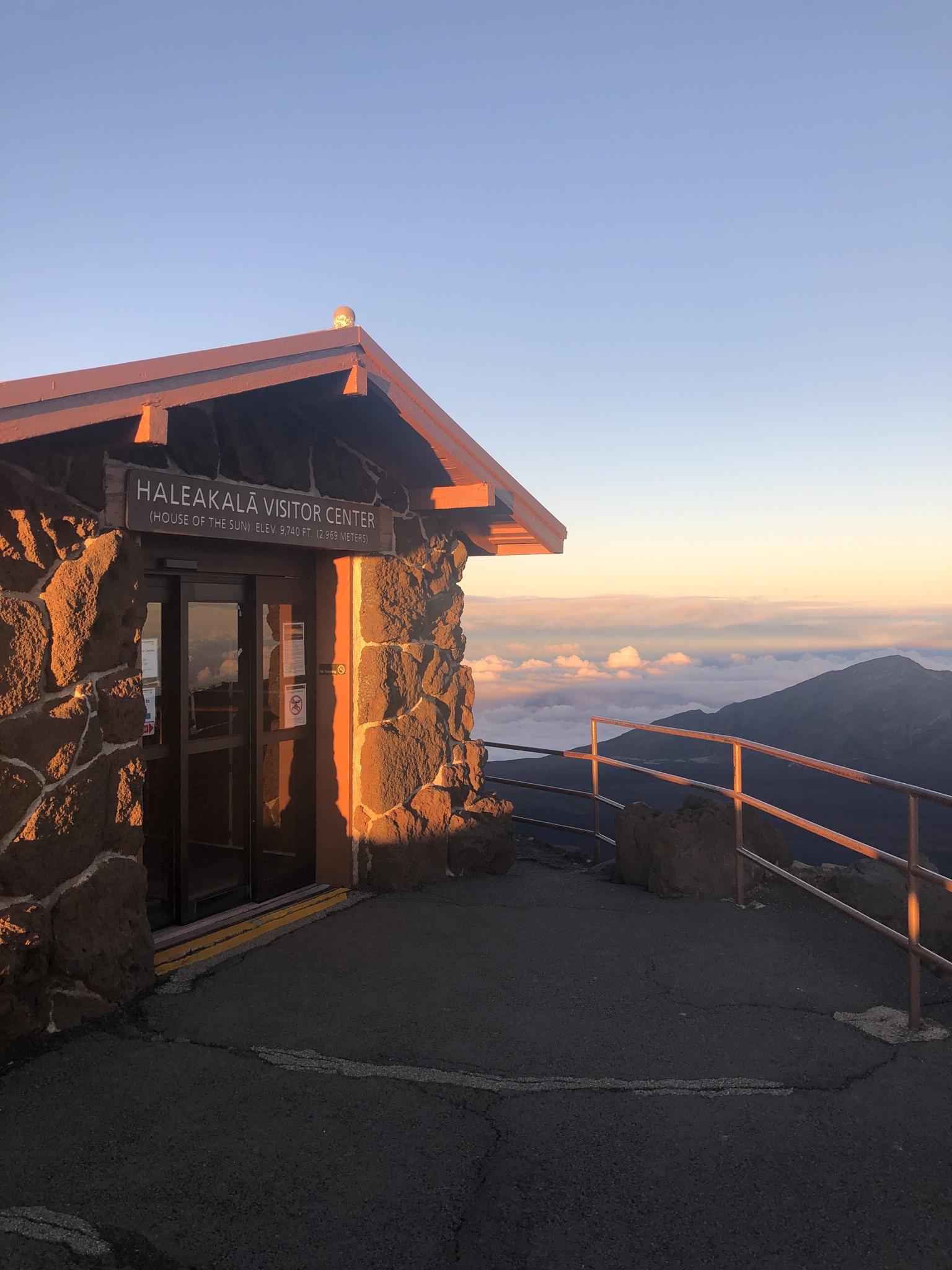 Stone visitor center at sunrise/sunset with clouds below a mountain peak.