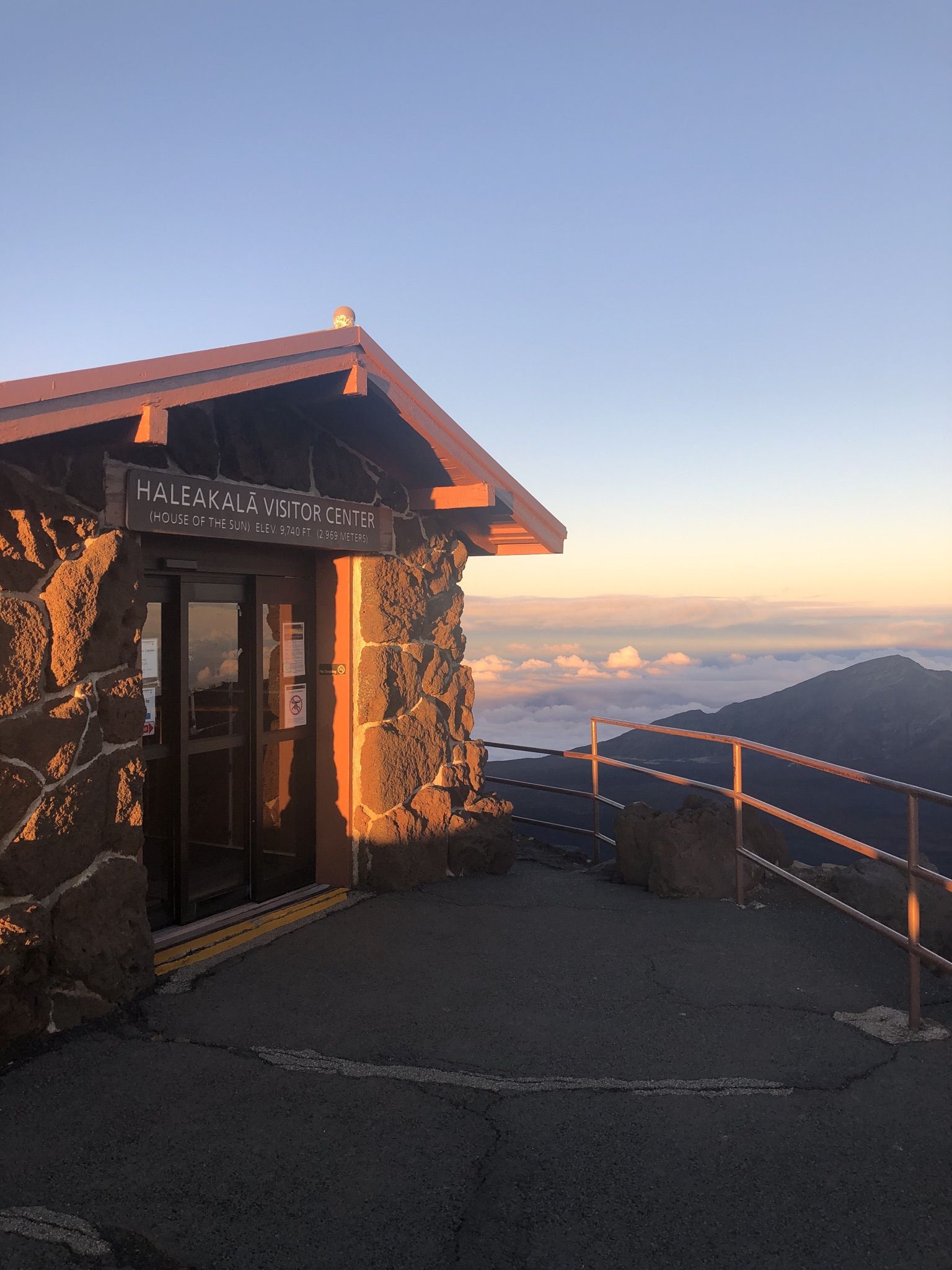 Stone visitor center at sunrise/sunset with clouds below a mountain peak. - Paia to Haleakalā (Cycle to the Sun)