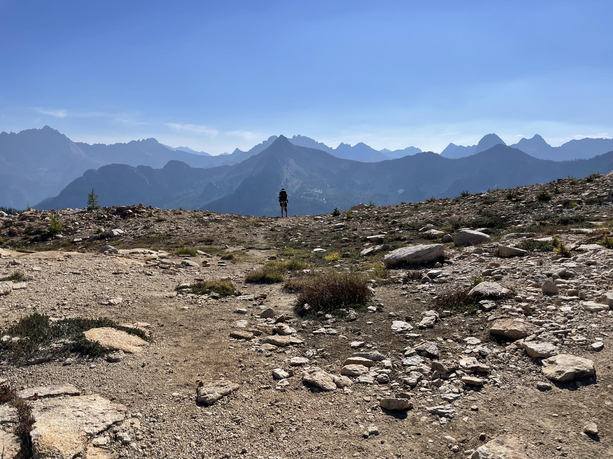 A person stands on a rocky mountain ridge overlooking distant peaks.