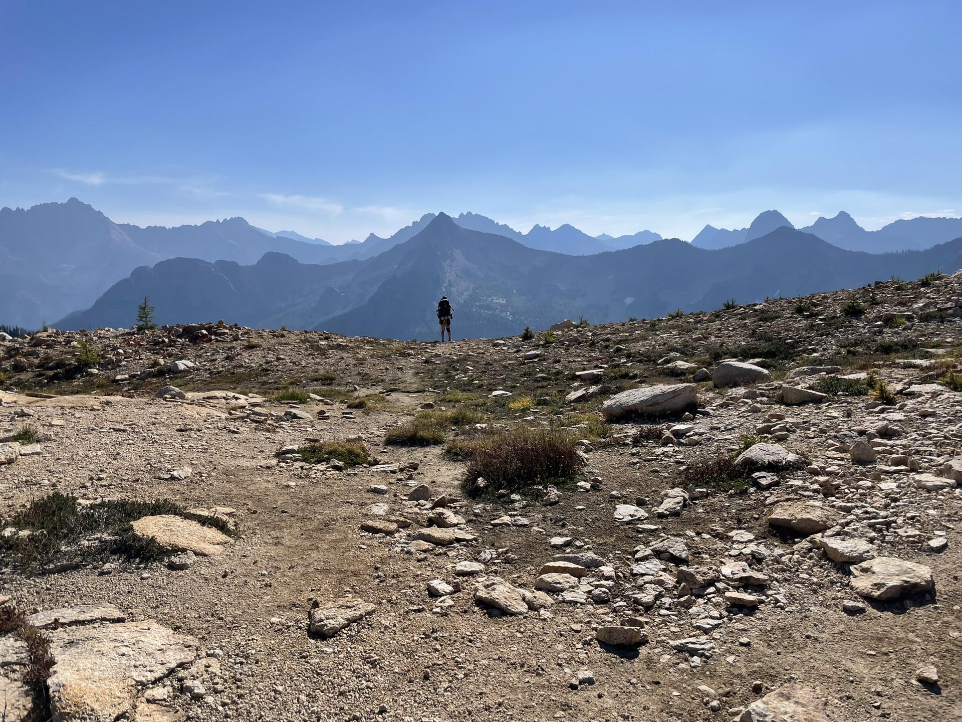 A person stands on a rocky mountain ridge overlooking distant peaks.