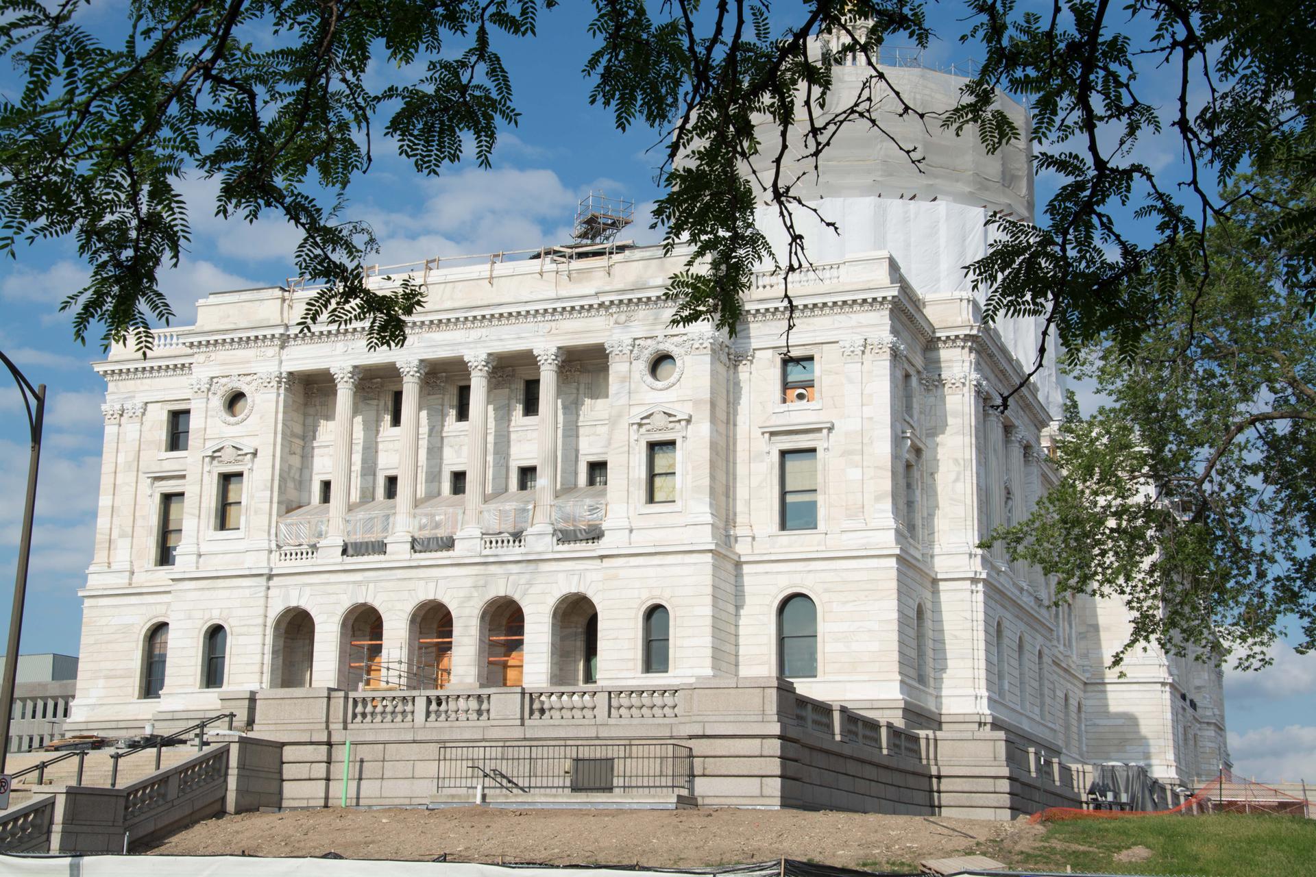 Grand white stone building with columns, dome under construction, framed by trees.