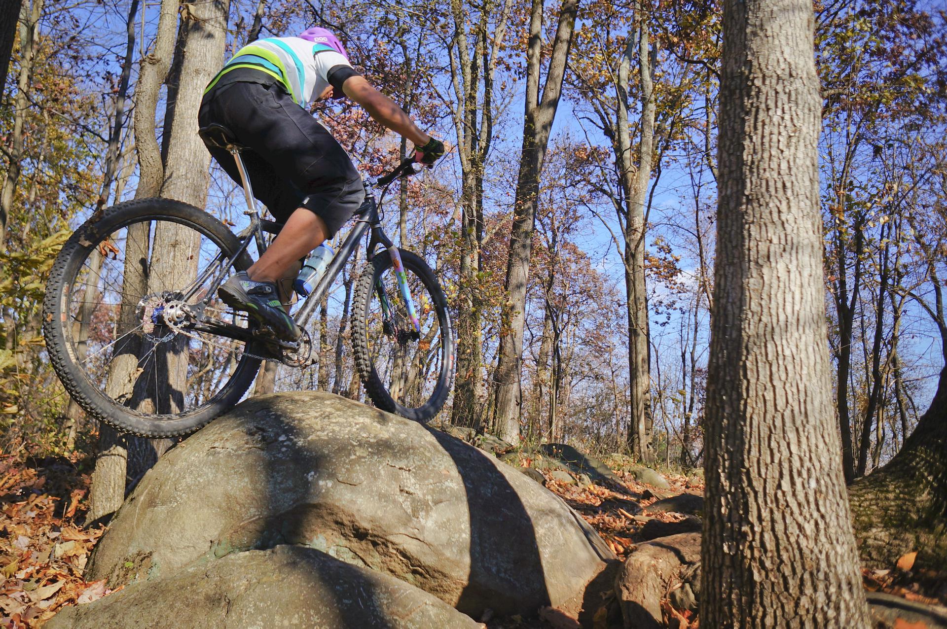 Mountain biker on large rocks in a sunlit, autumn forest.