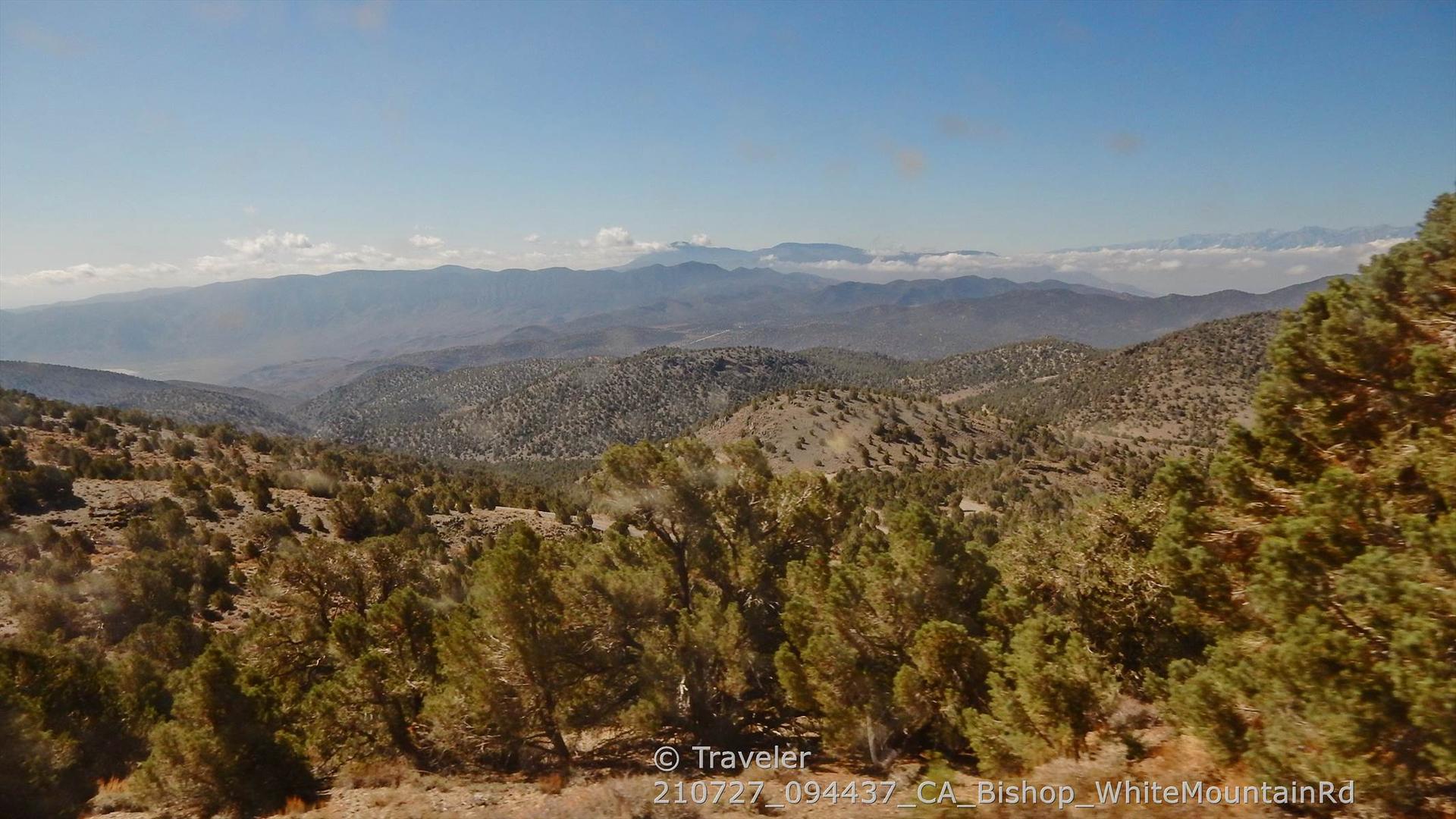 Panoramic view of forested mountains and valleys under a clear blue sky.