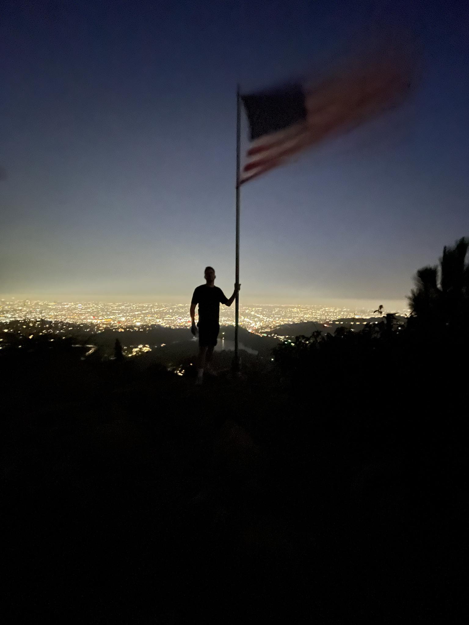 Silhouette of a person holding a flag against a city skyline at dusk.