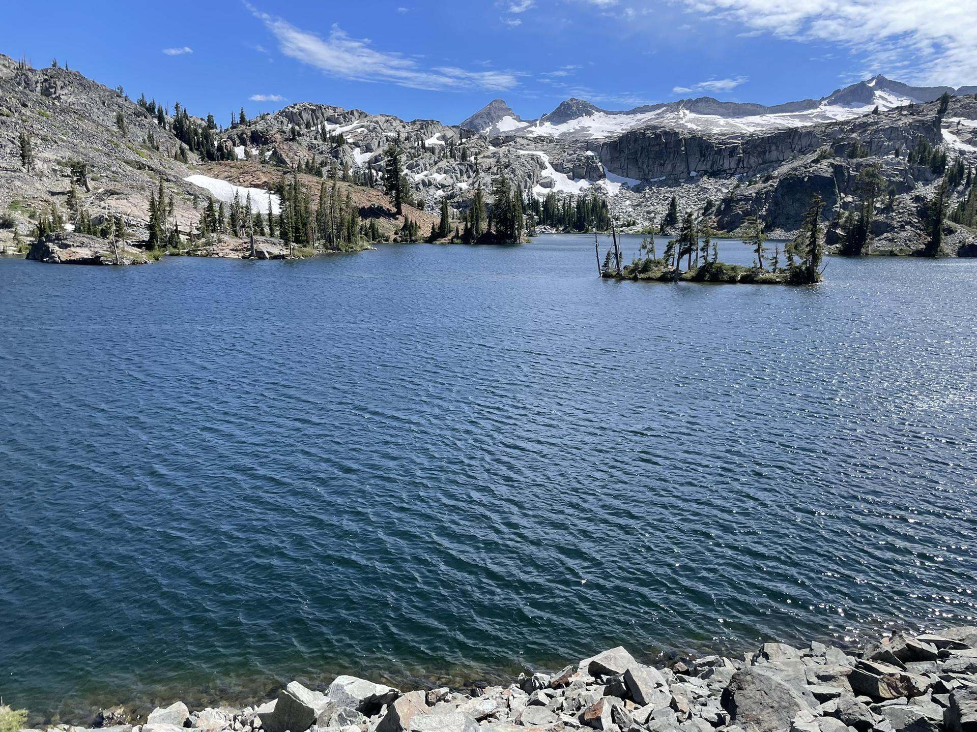 Blue lake with small islands and snow-capped mountains under a partly cloudy sky.